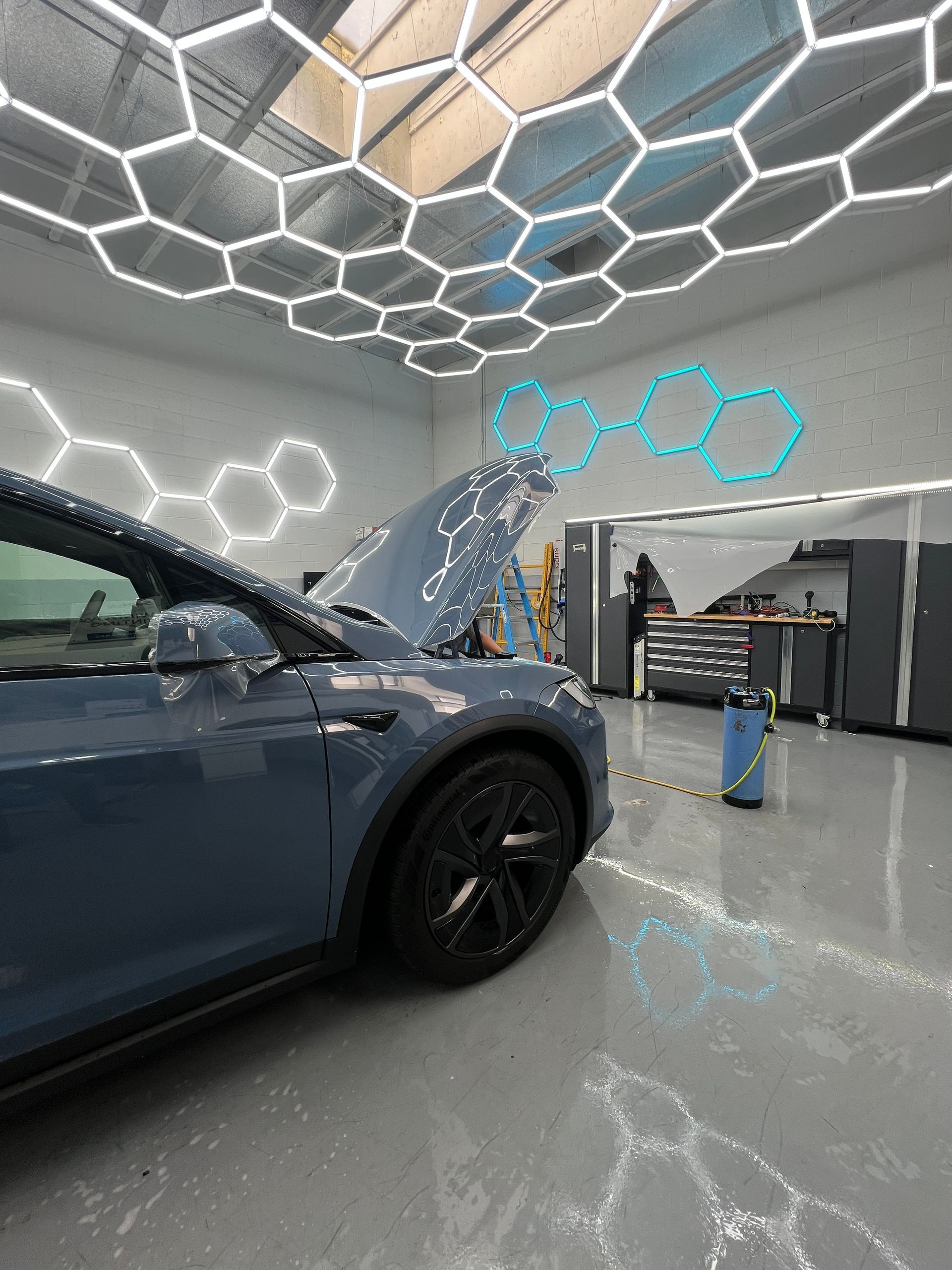 Blue sports car in a futuristic showroom with hexagonal ceiling lights reflecting on the floor
