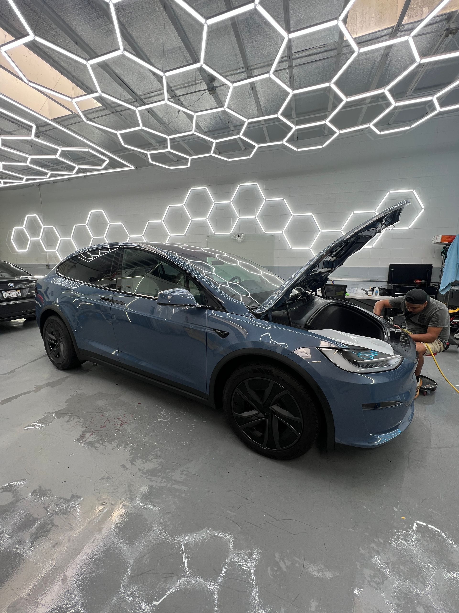 Blue SUV with hood open in a futuristic garage, a mechanic working beside it