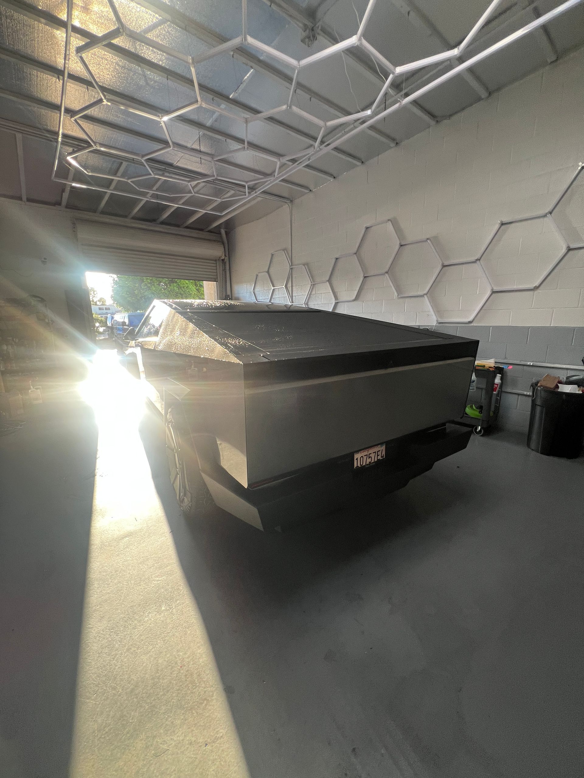 Black boat or trailer parked inside a modern garage with hexagonal wall and ceiling panels.