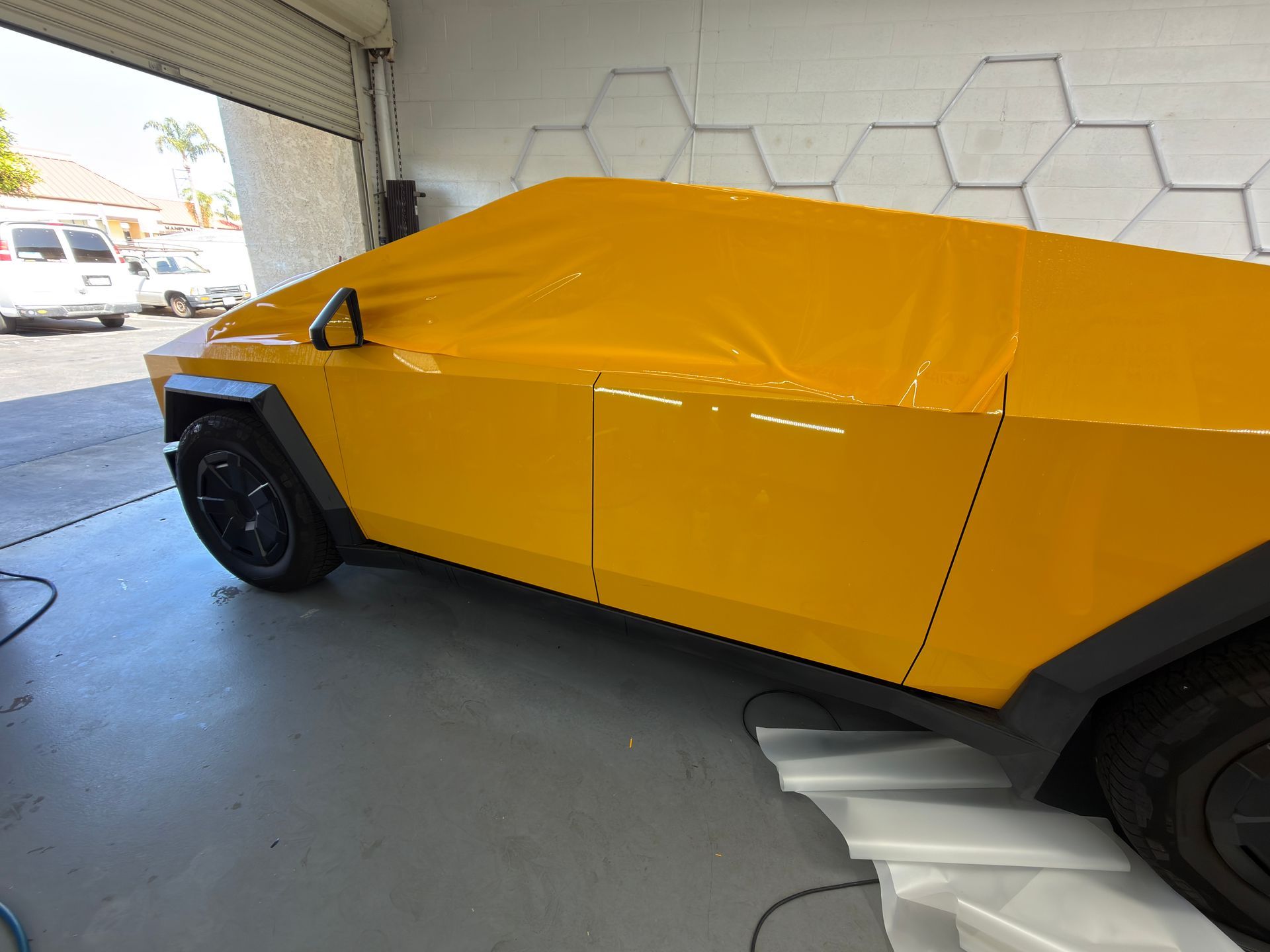 Yellow angular sports car in a garage, side view with cover over the body