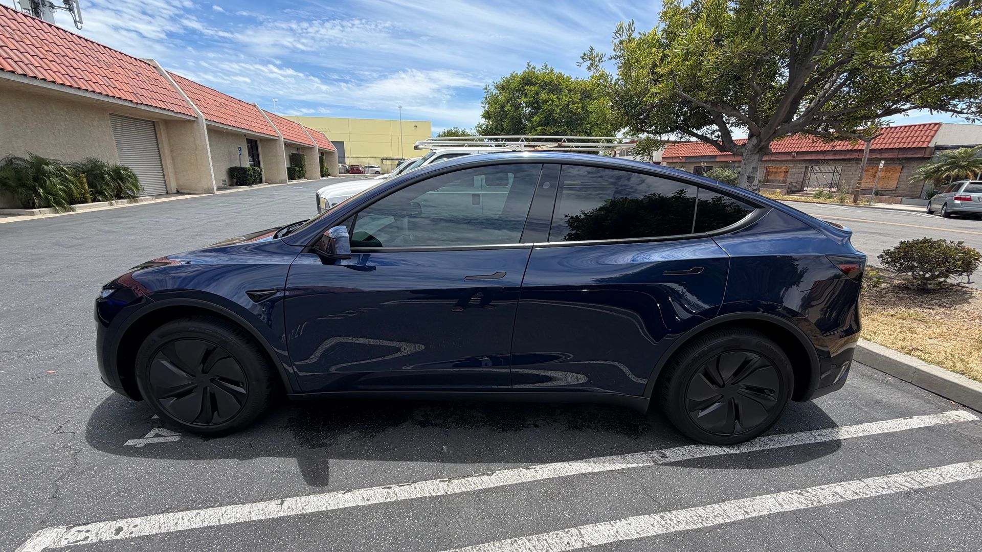 Blue SUV parked in a lot beside a sidewalk and building under a sunny sky