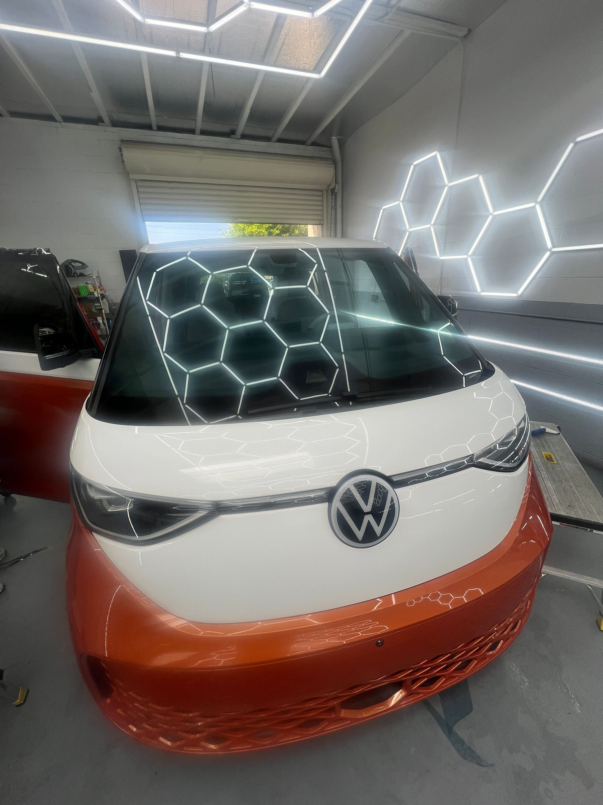 Volkswagen van with white roof and orange front in a garage, reflected by hexagonal LED lights on windshield