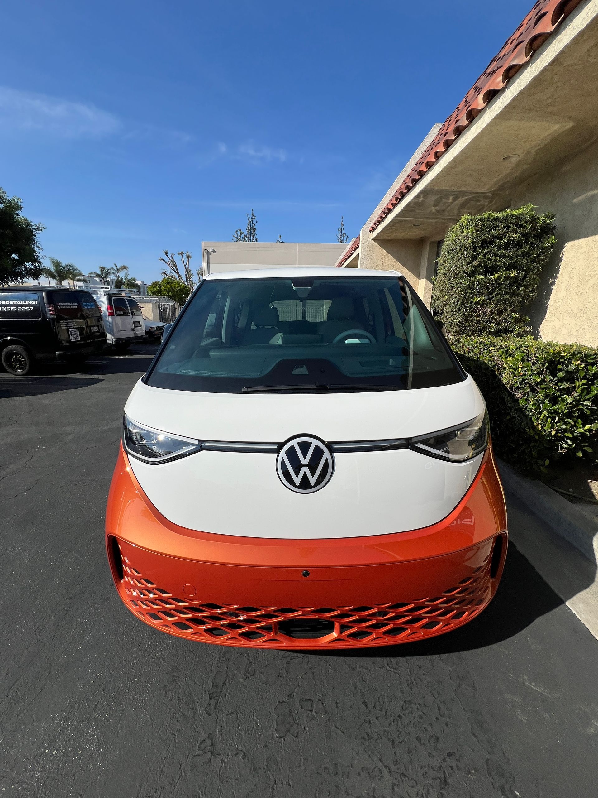 Front view of a white and orange Volkswagen parked outdoors in a sunny lot