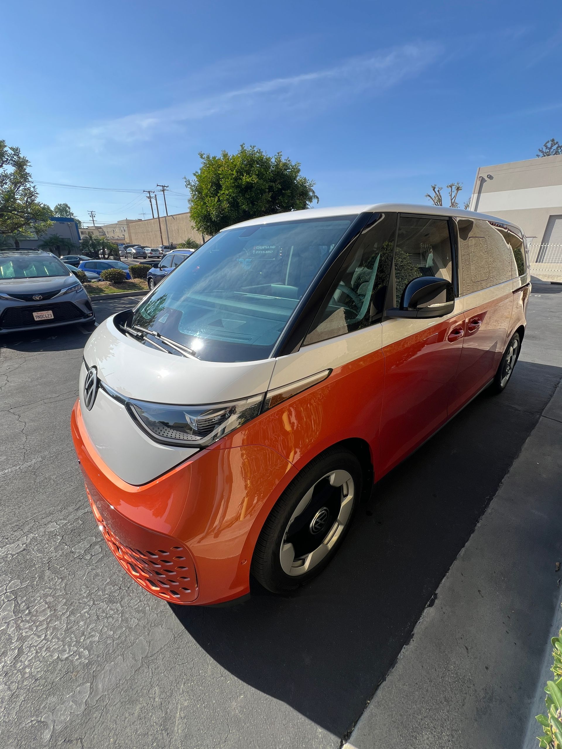 Orange and white compact electric van parked outdoors under a blue sky
