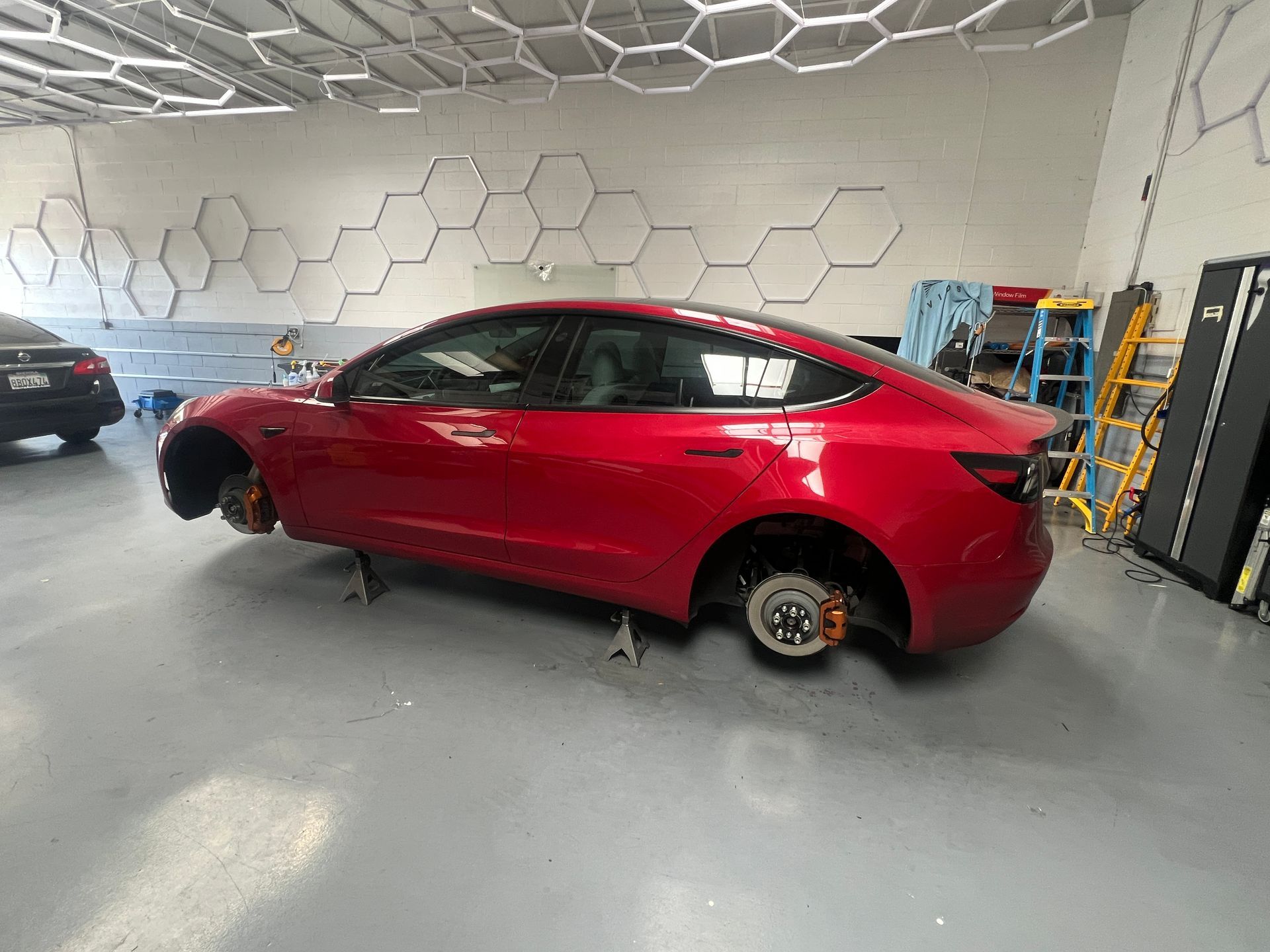 Red sedan in a garage with one wheel removed, showing a brake rotor.