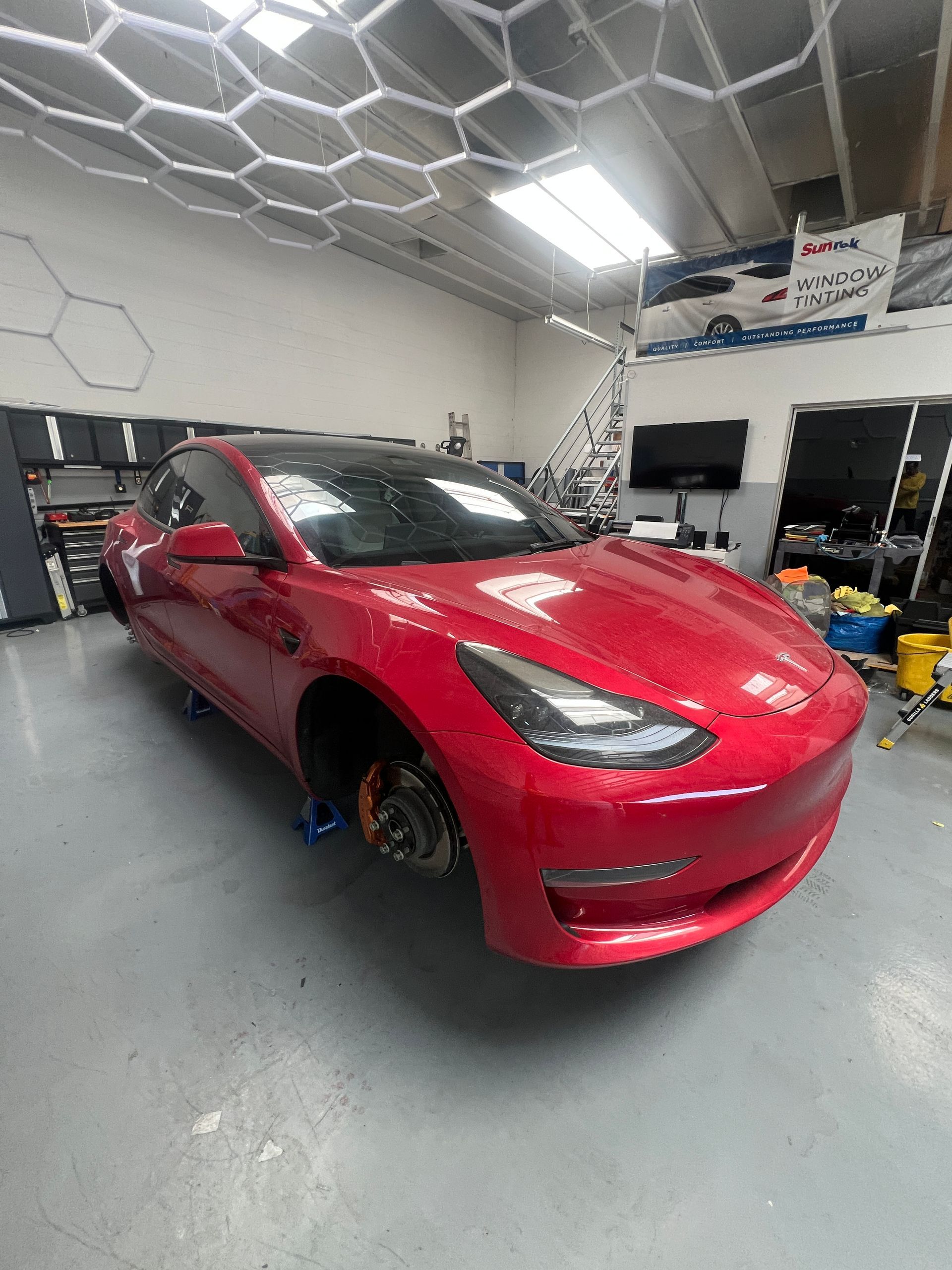 Red Tesla sedan in an auto shop garage with one front wheel removed