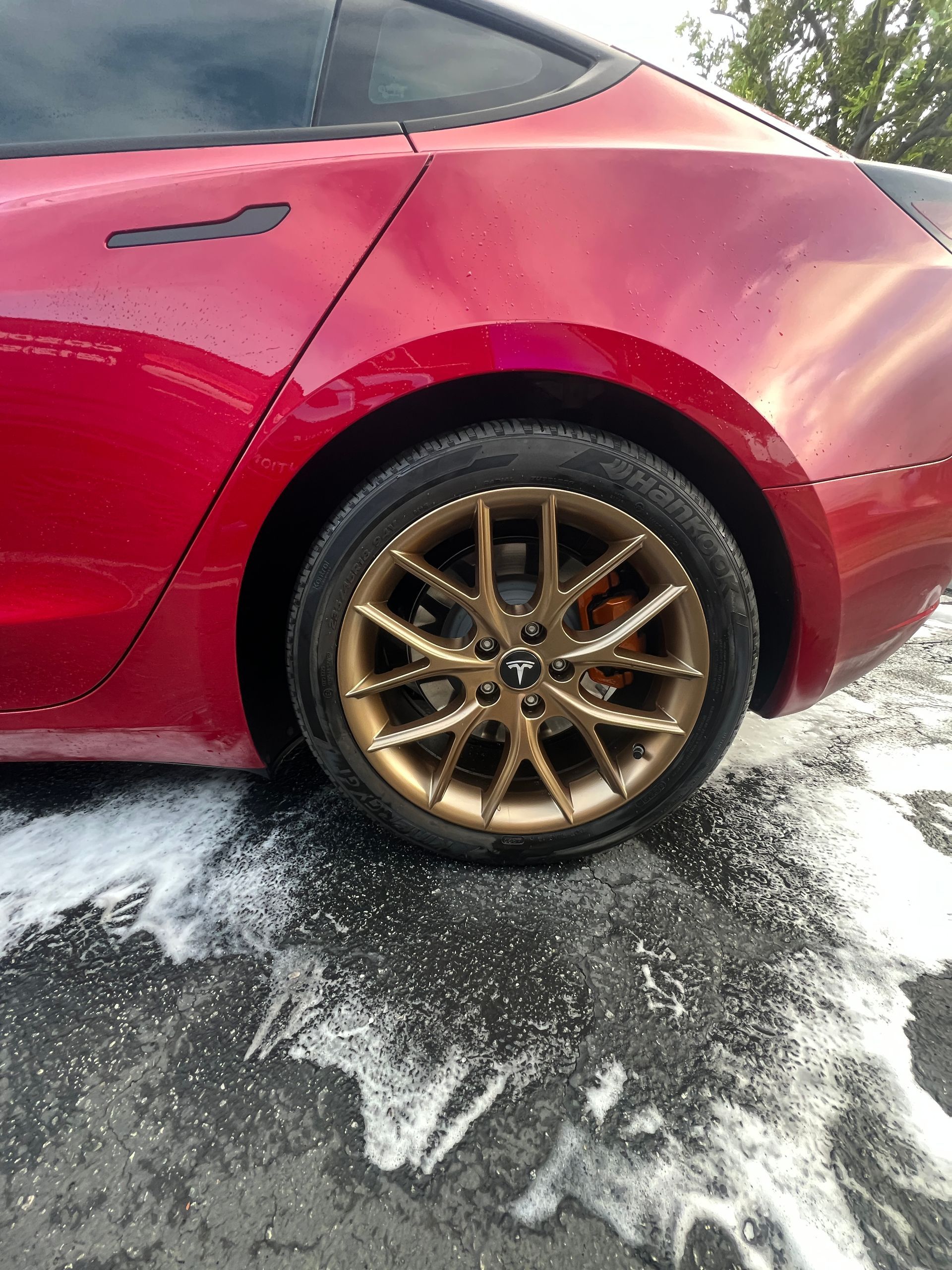 Red car rear wheel with bronze rim parked on wet, snowy pavement