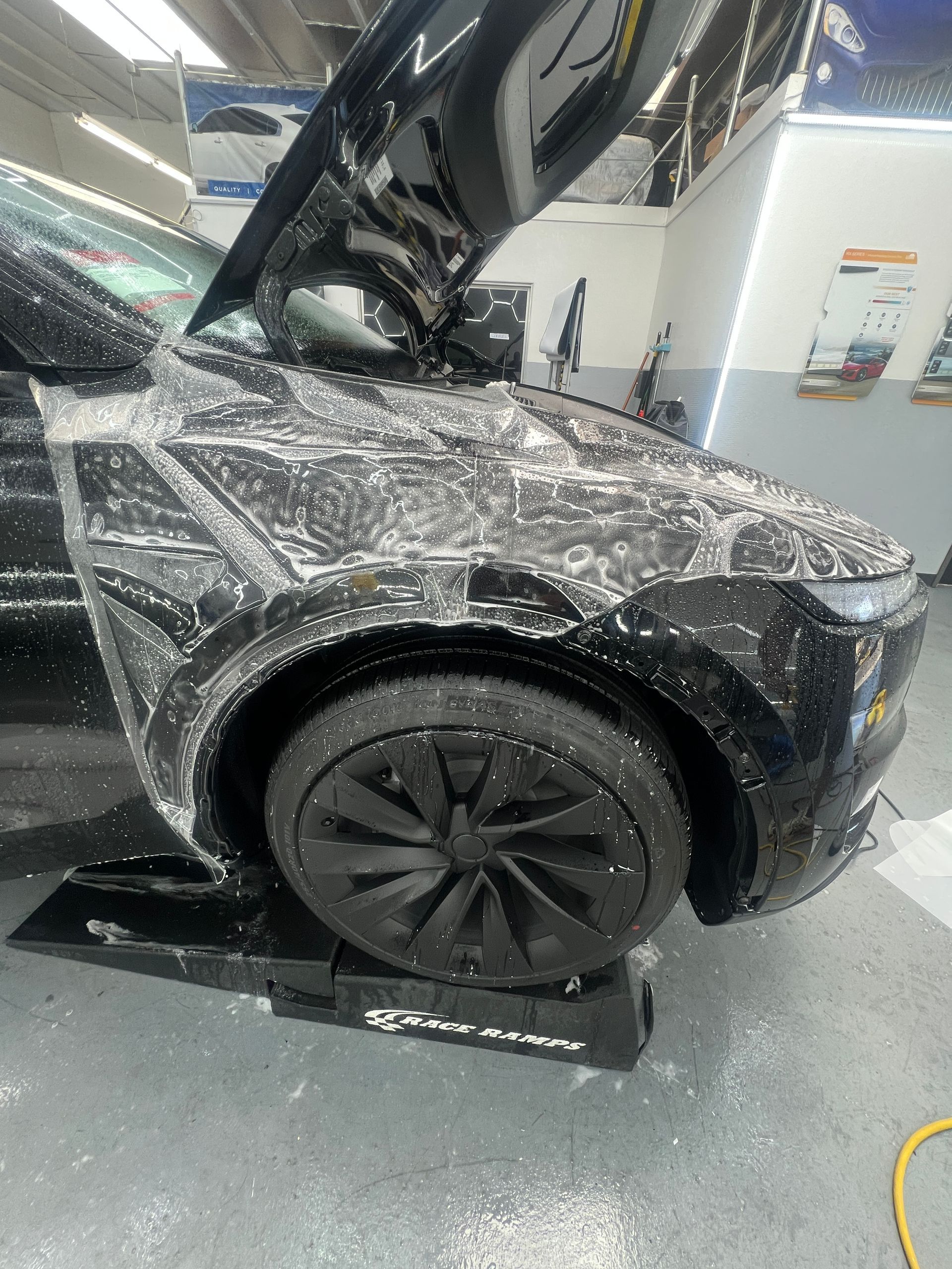 Wrapped black car with hood open in an auto shop
