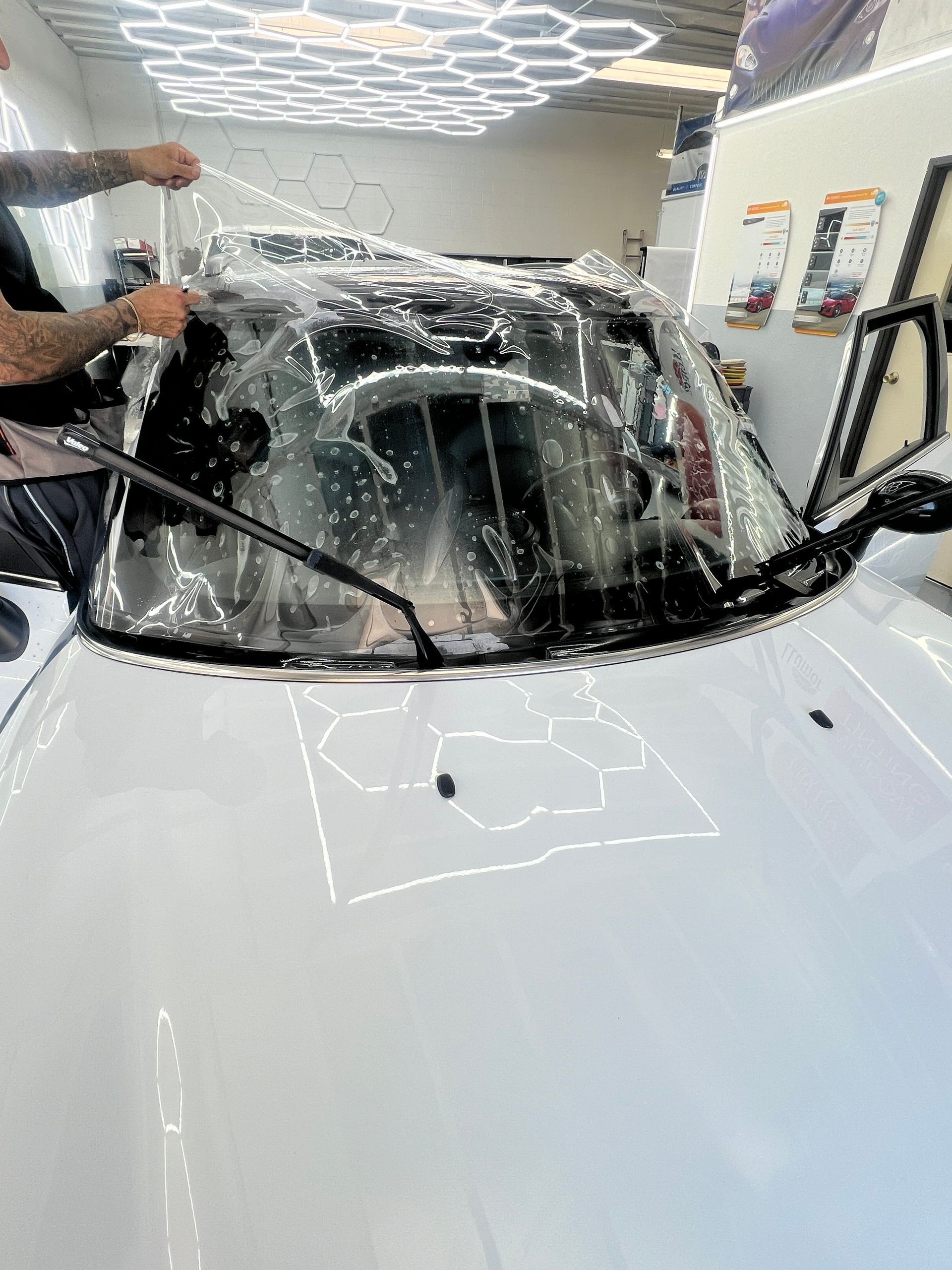 Person washing a white car’s windshield with soap in an auto detailing shop