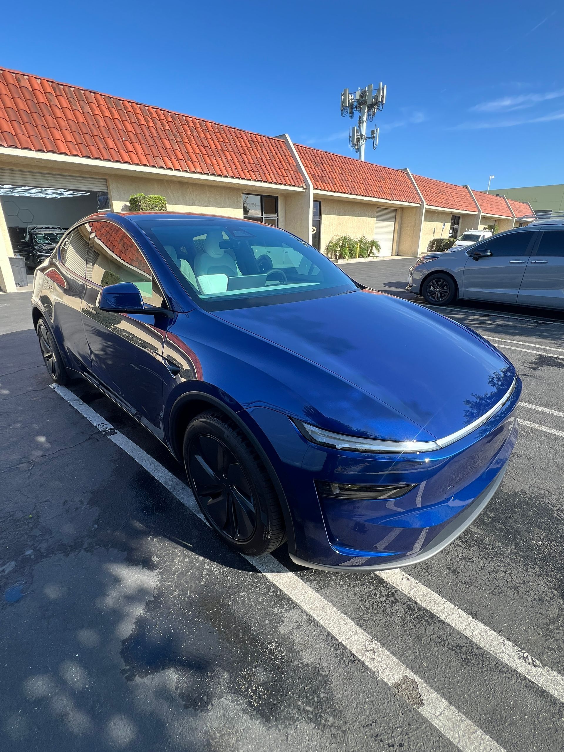 Blue SUV parked in a lot beside a red-roofed building under a clear sky