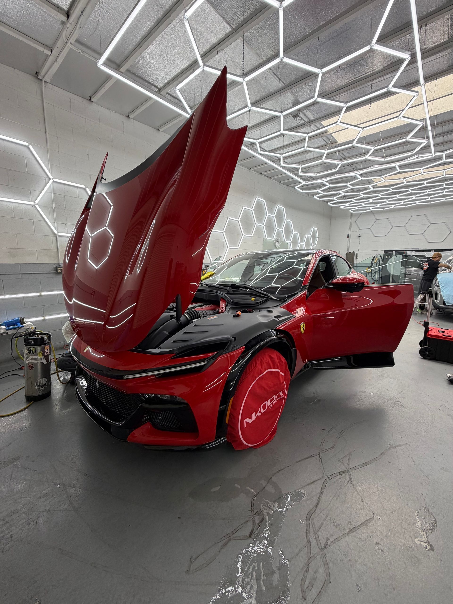 Red sports car with open hood and doors in a bright showroom with hexagonal ceiling lights