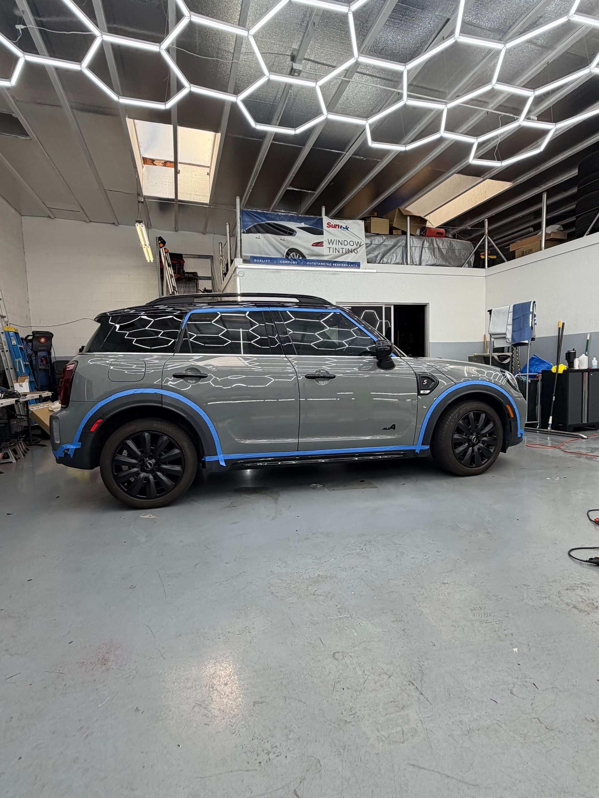Silver Mini Cooper with blue accents parked inside a modern auto shop under hexagonal ceiling lights