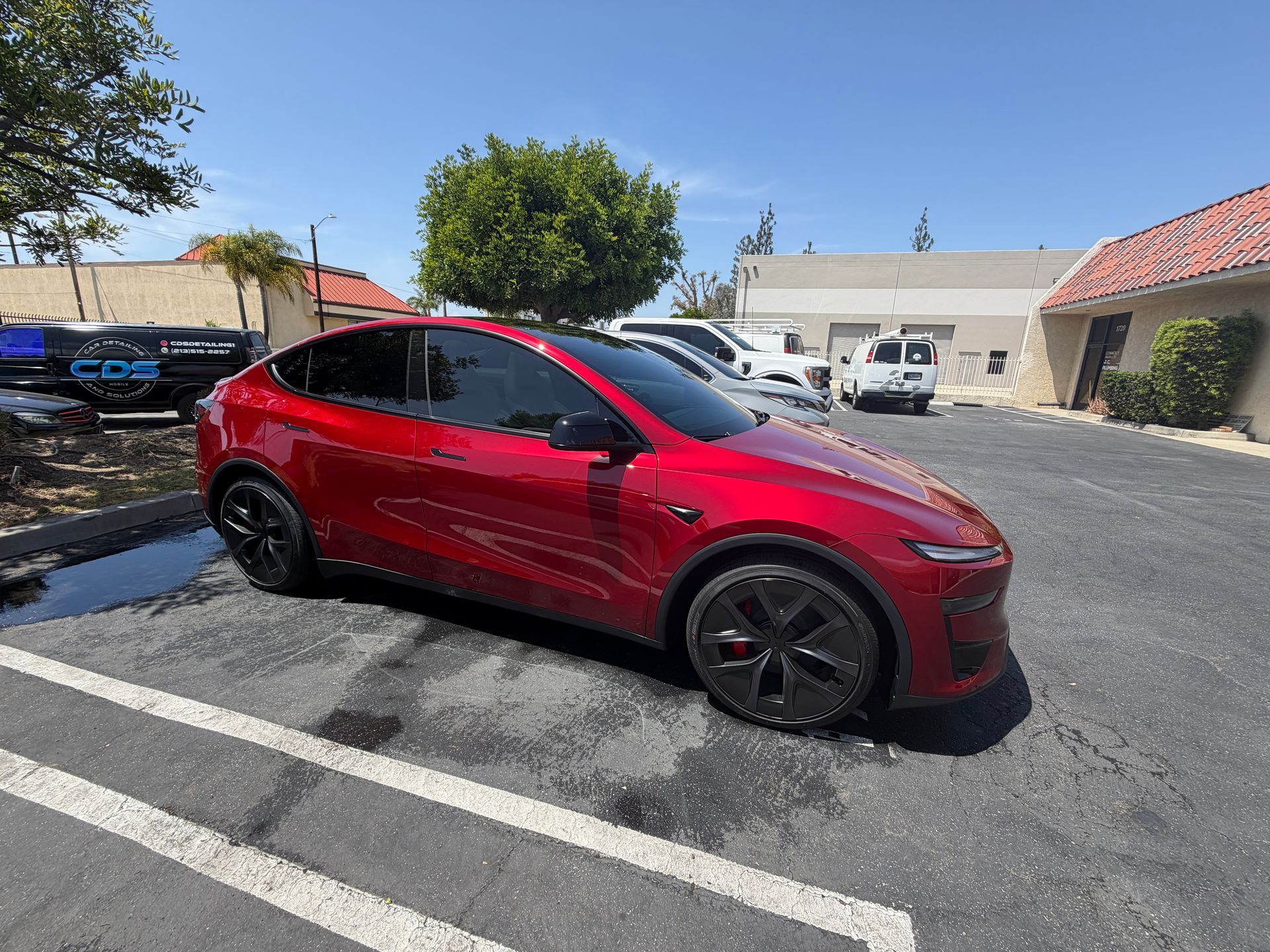 Red sports sedan parked in a sunny lot beside white buildings and other cars.