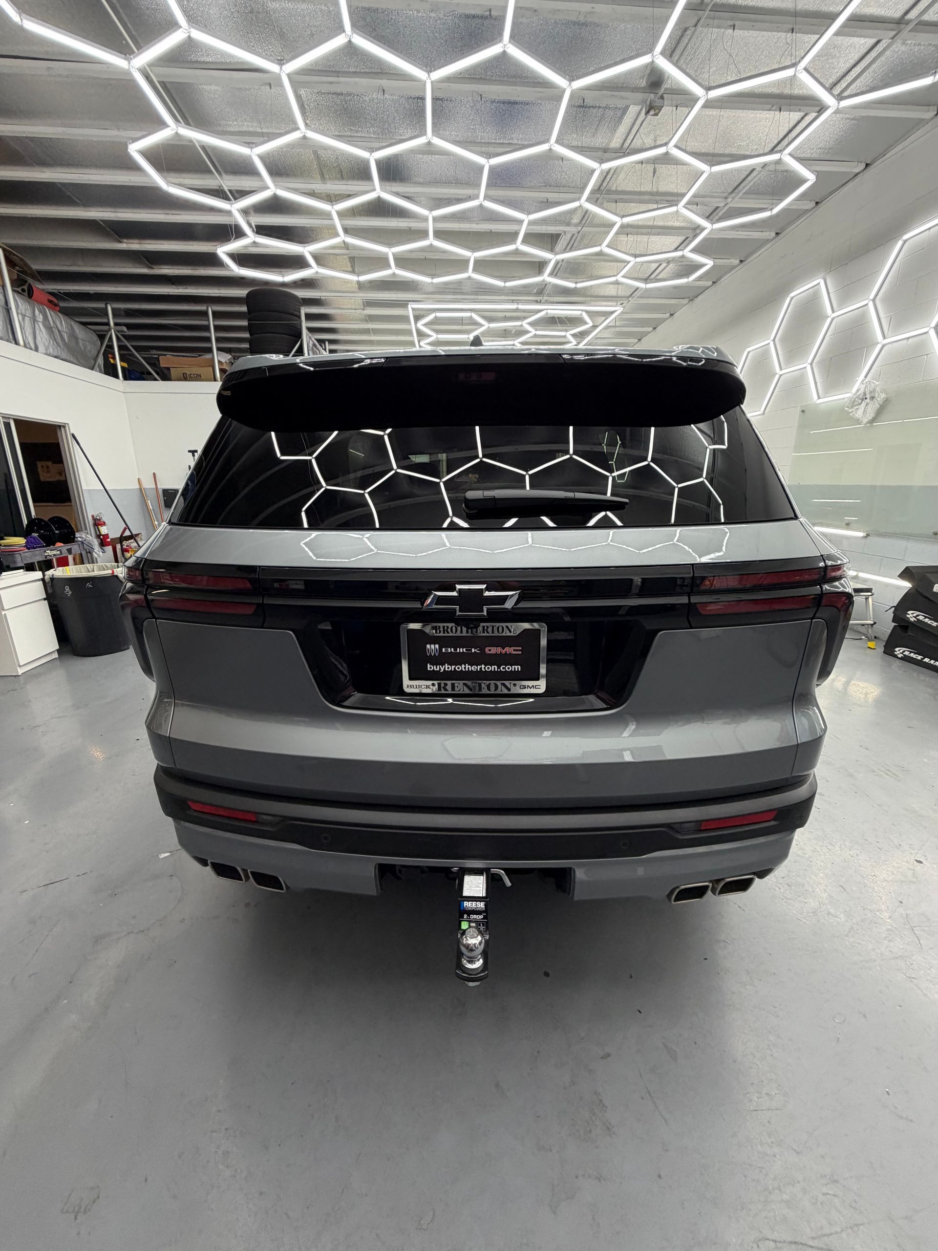Rear view of a gray SUV in a bright garage with hexagonal ceiling lights and a tow hitch attached