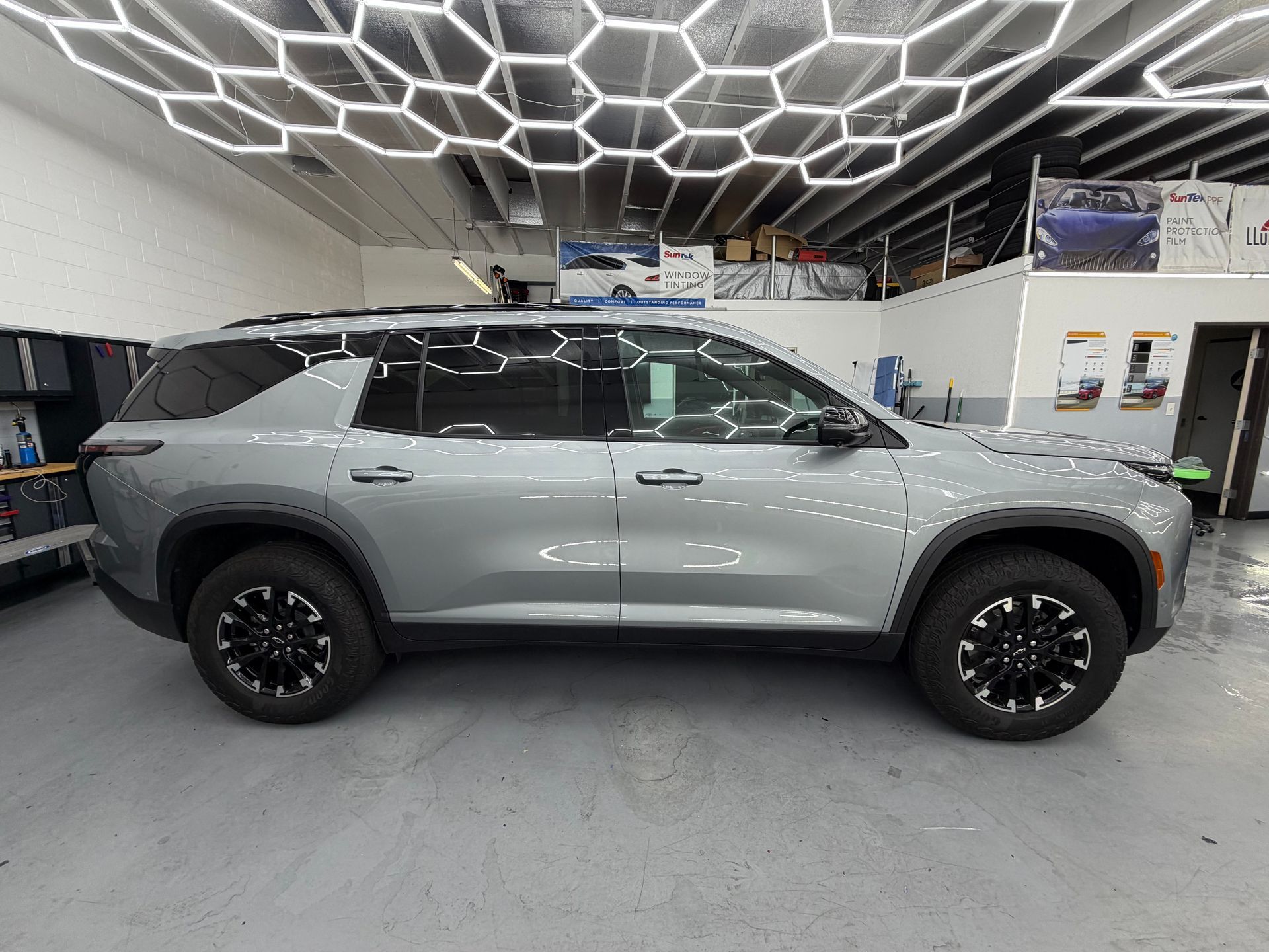 Gray SUV in a showroom with geometric ceiling lights, side view under bright indoor lighting