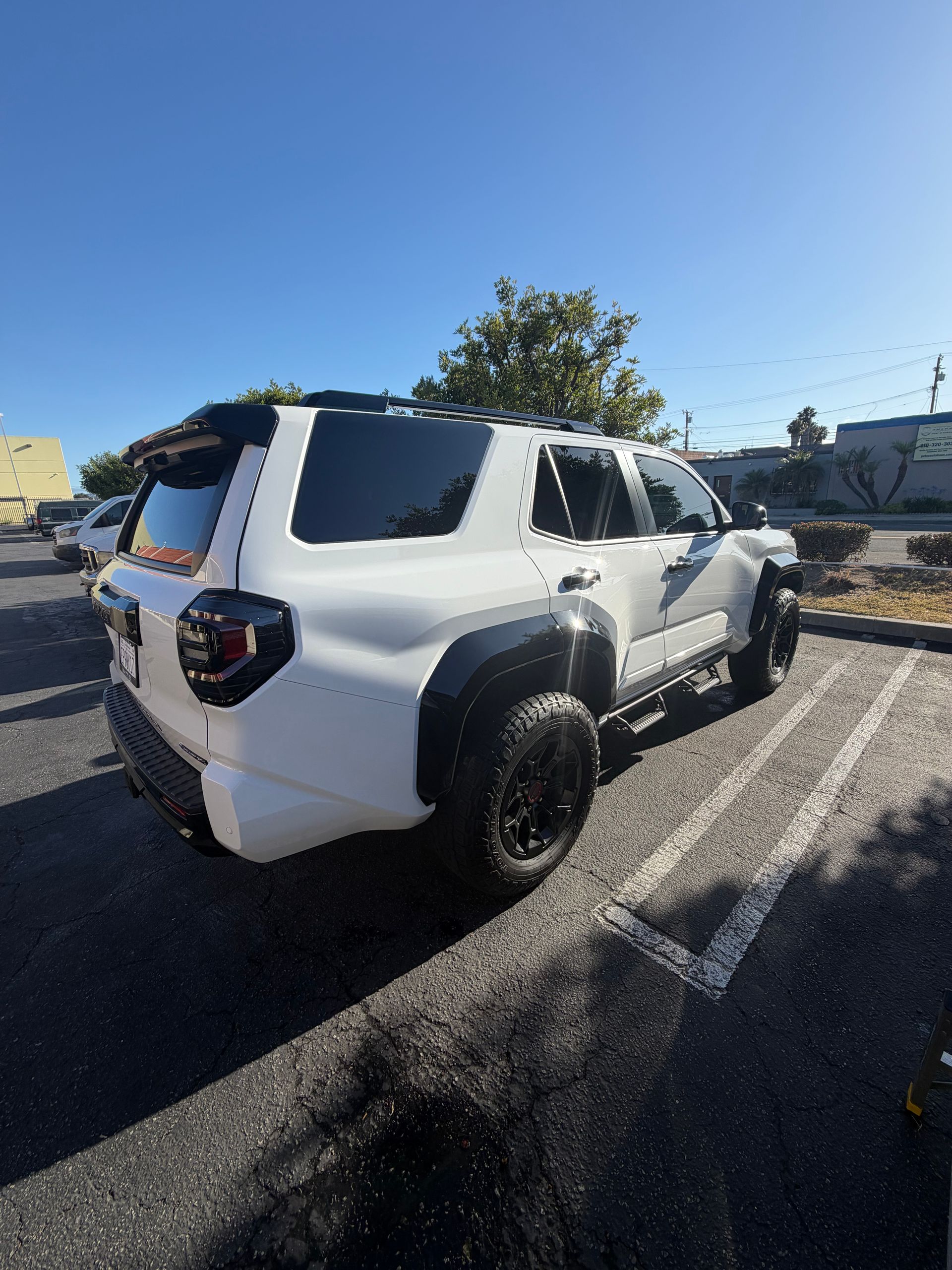 White SUV parked in a sunny parking lot, viewed from the rear side.
