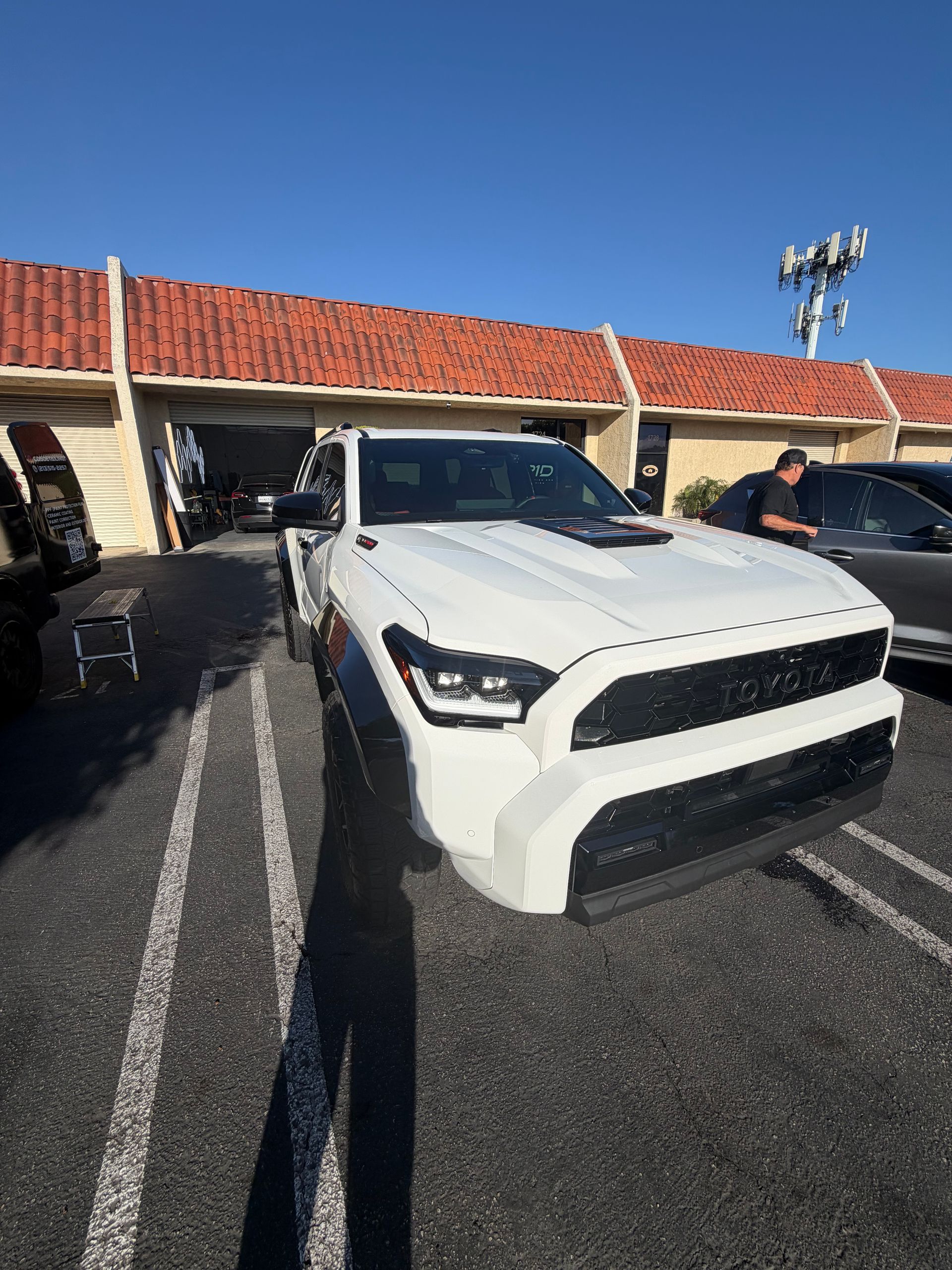 White pickup truck parked in a lot in front of a building with a red tile roof under a clear blue sky
