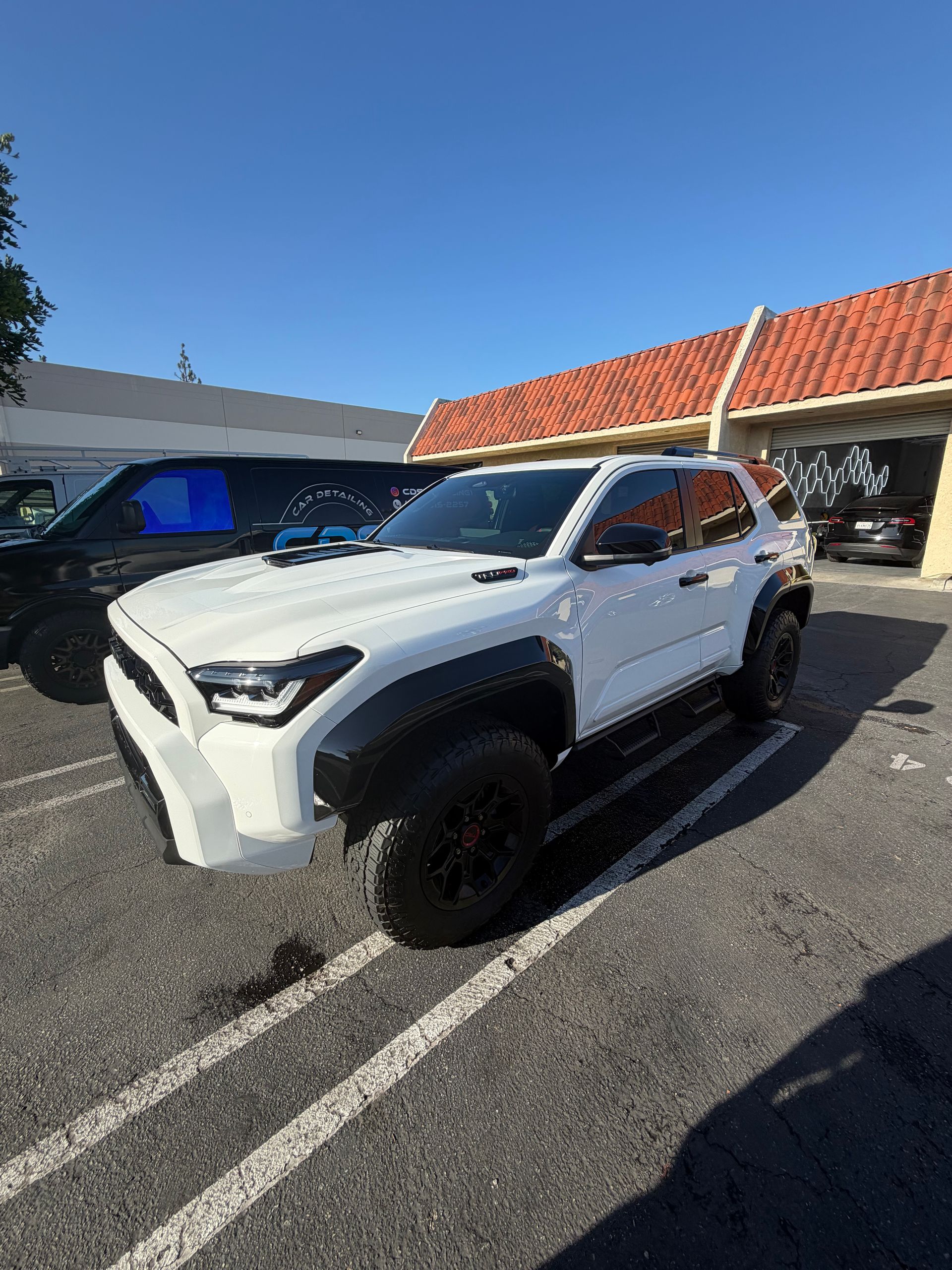 White SUV parked in a lot beside a black vehicle, with a building and blue sky in the background.