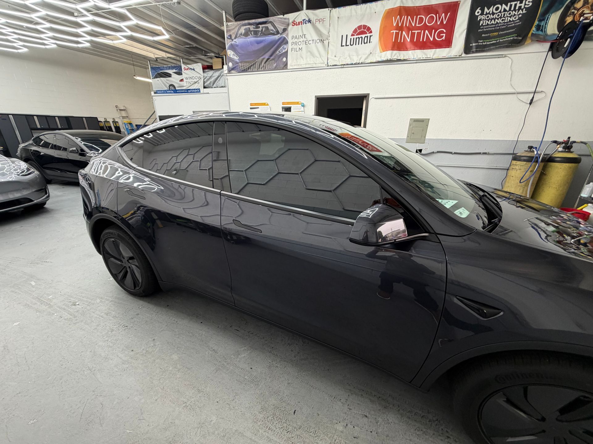 Black sedan parked indoors in an auto shop, side view with tinted windows and black wheels