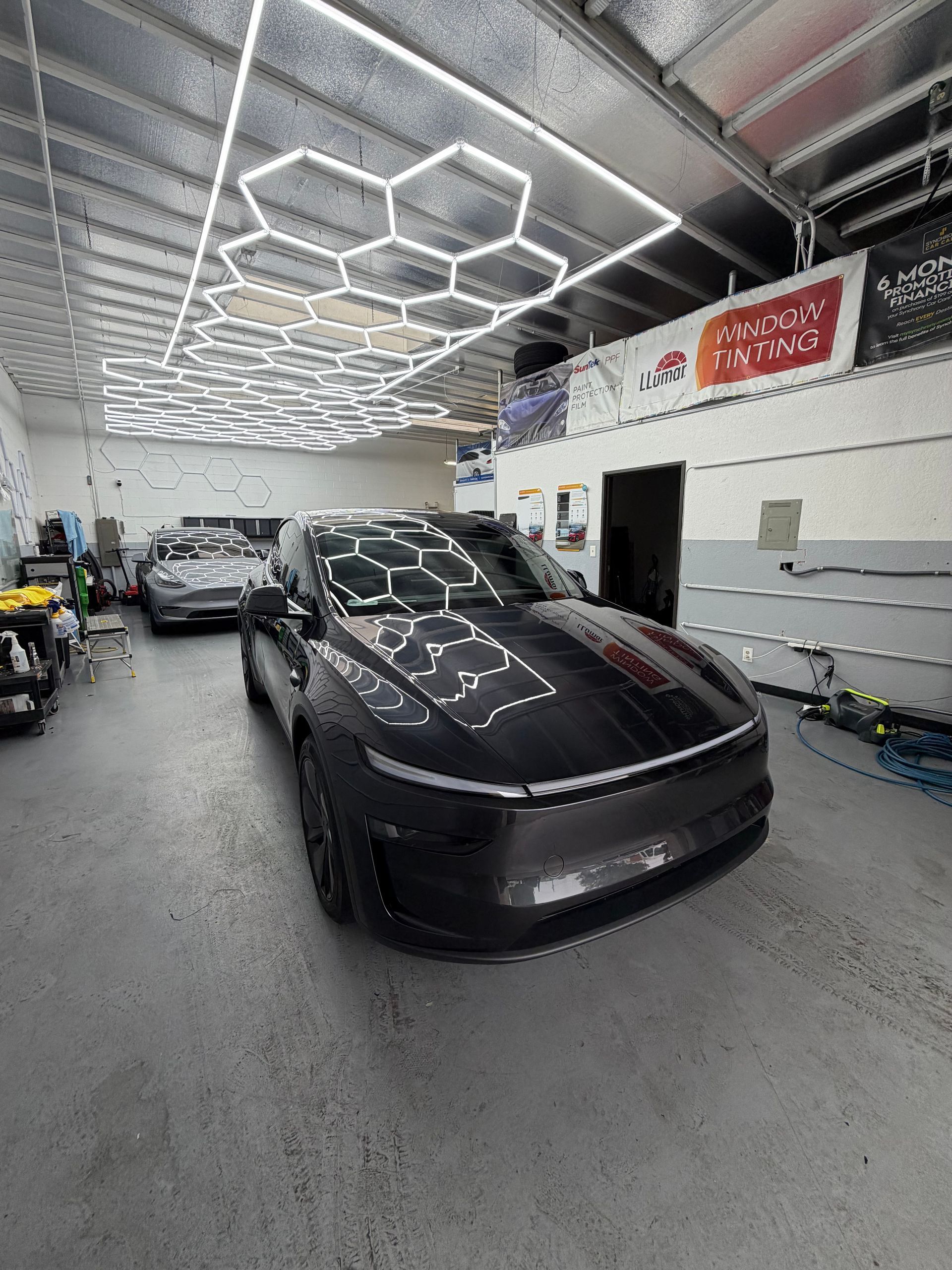 Black car in an auto shop with hexagonal LED ceiling lights reflecting on the hood