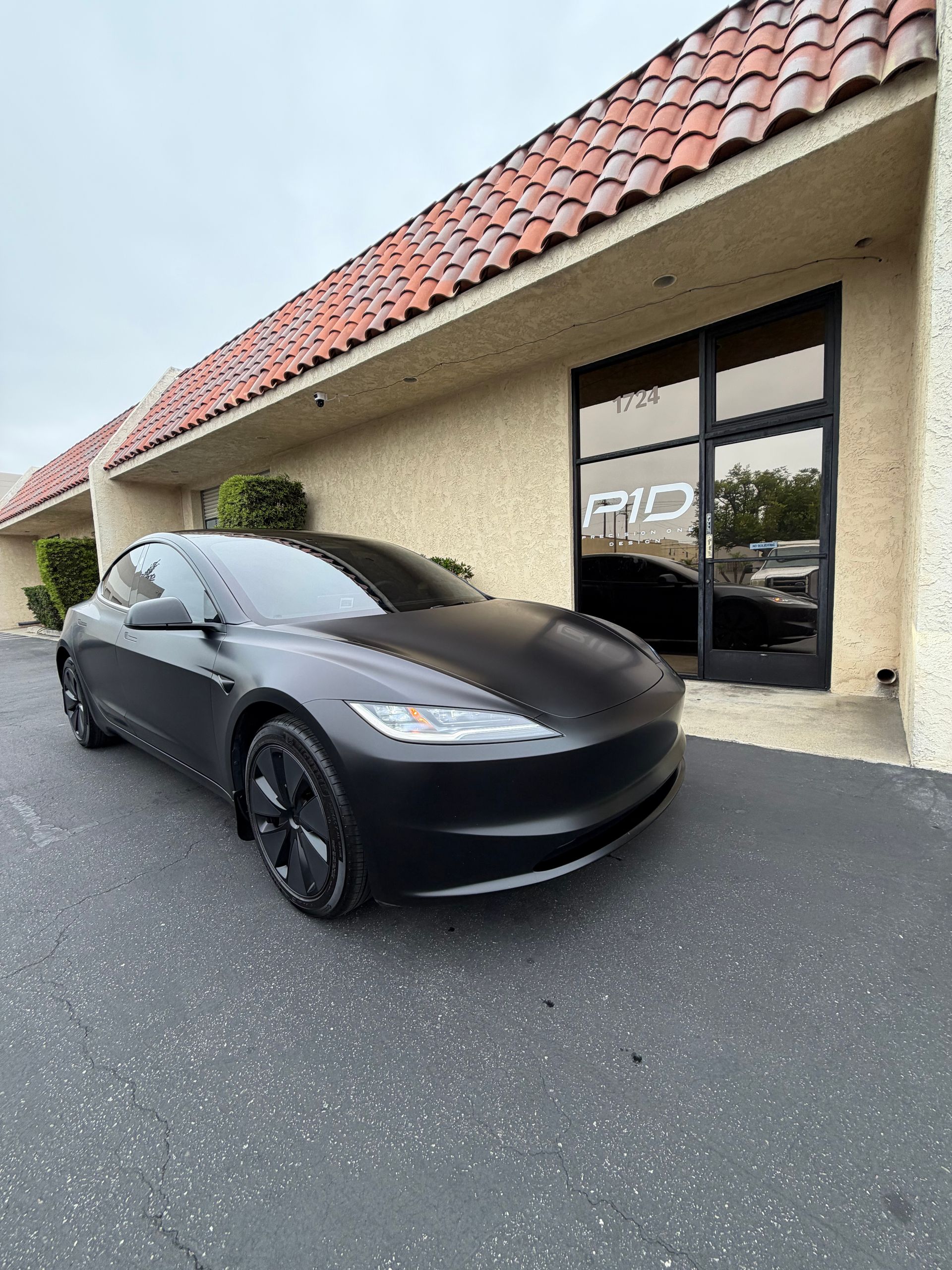 Black sedan parked outside a beige storefront with a red tile roof.