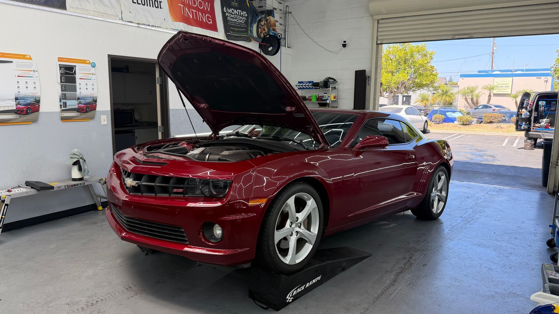 Red sports coupe in a garage with hood open, on a lift or ramp.