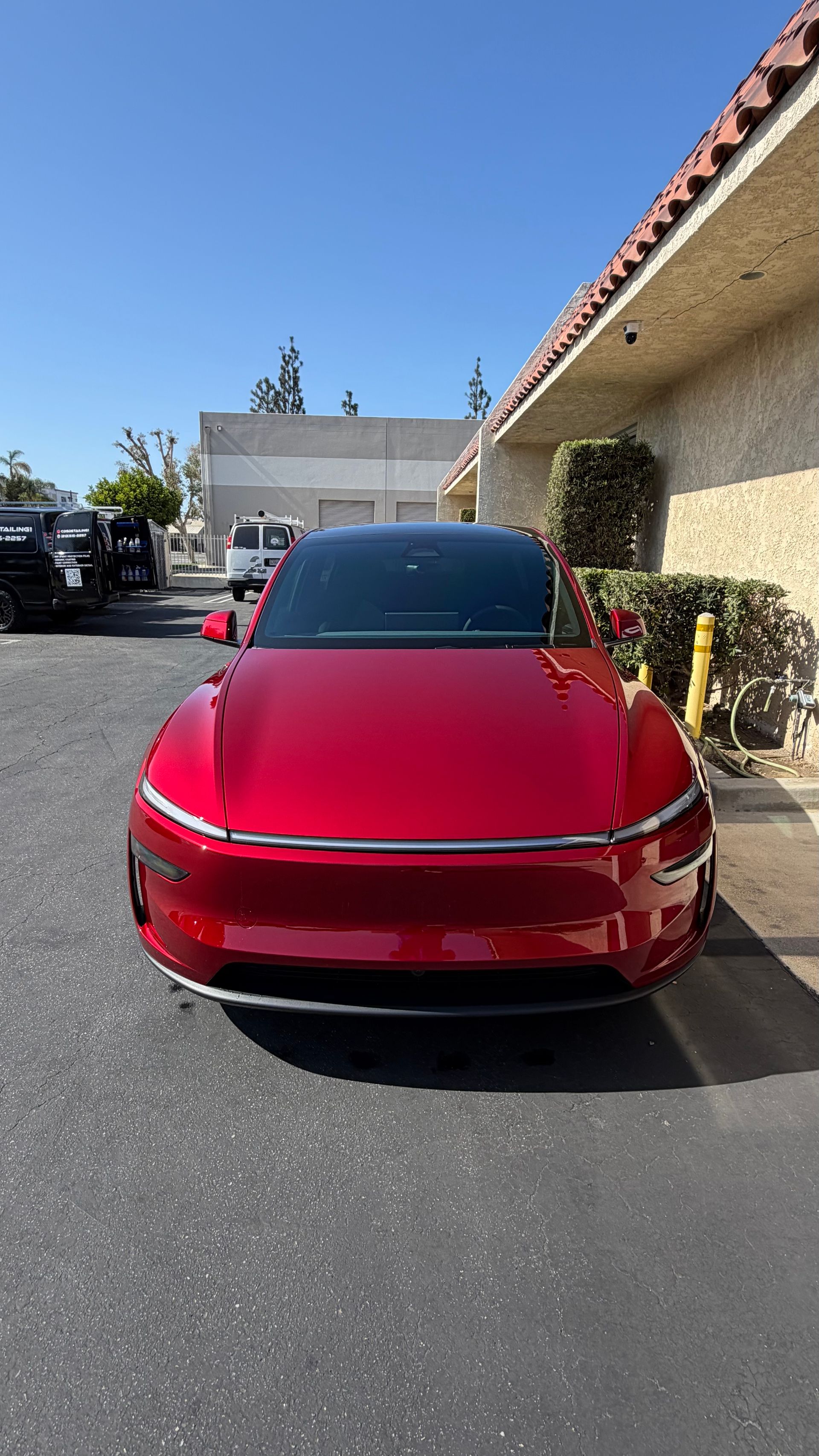 Red car parked in a lot beside a stucco building on a sunny day