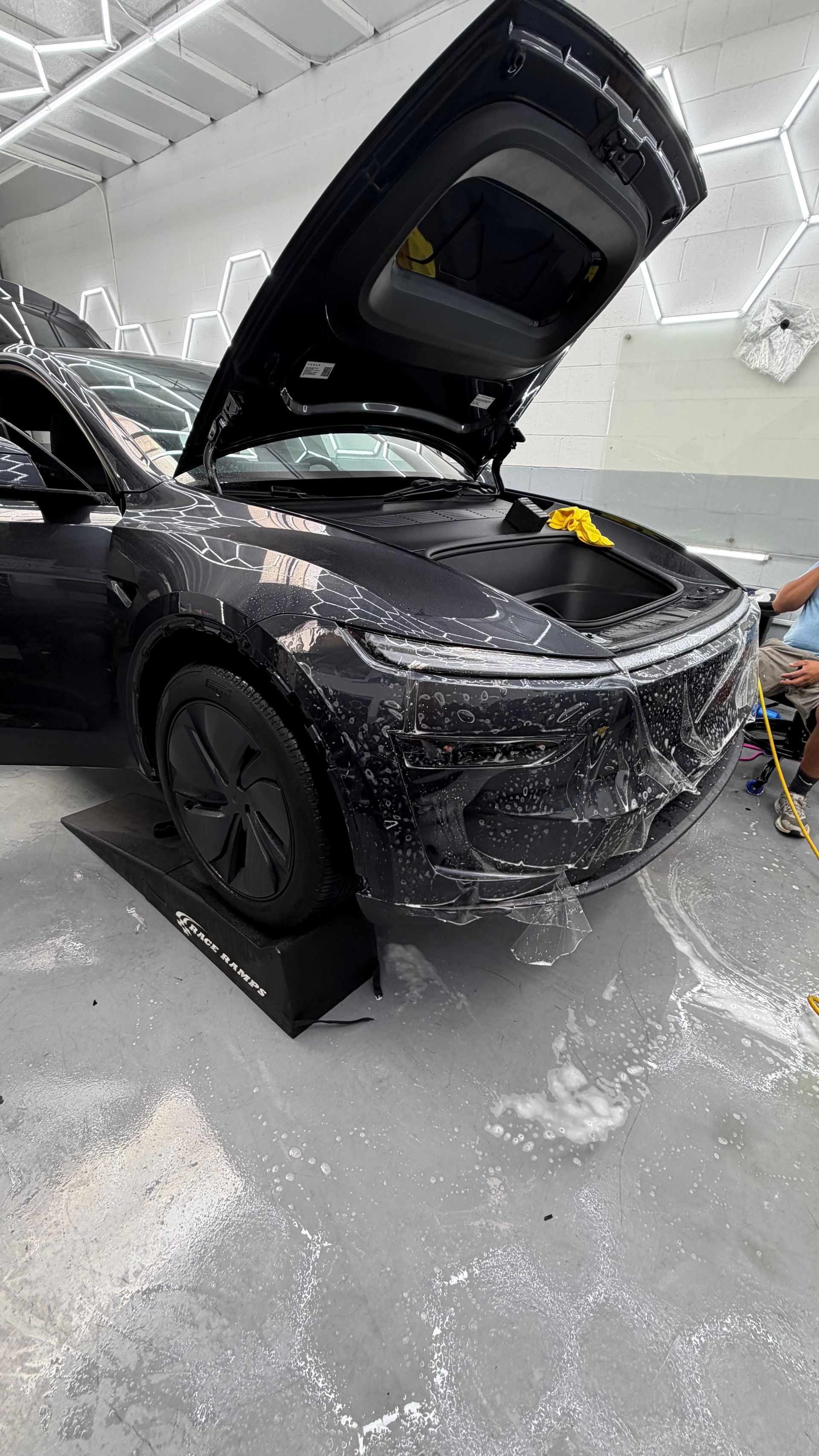 Black SUV in a showroom, hood open with protective wrap around the front.