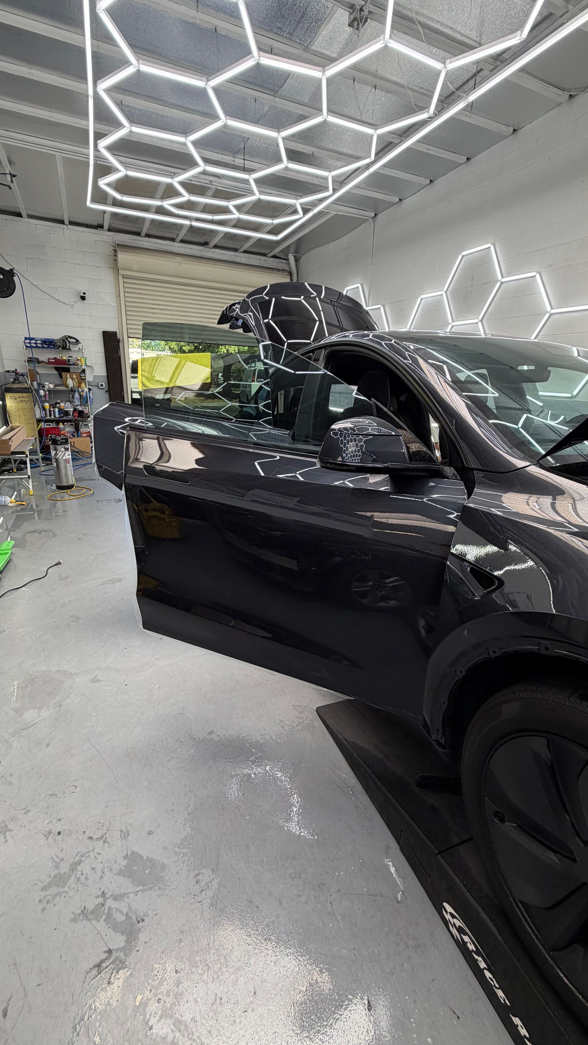 Black SUV in an auto shop with its door open under bright hexagonal ceiling lights