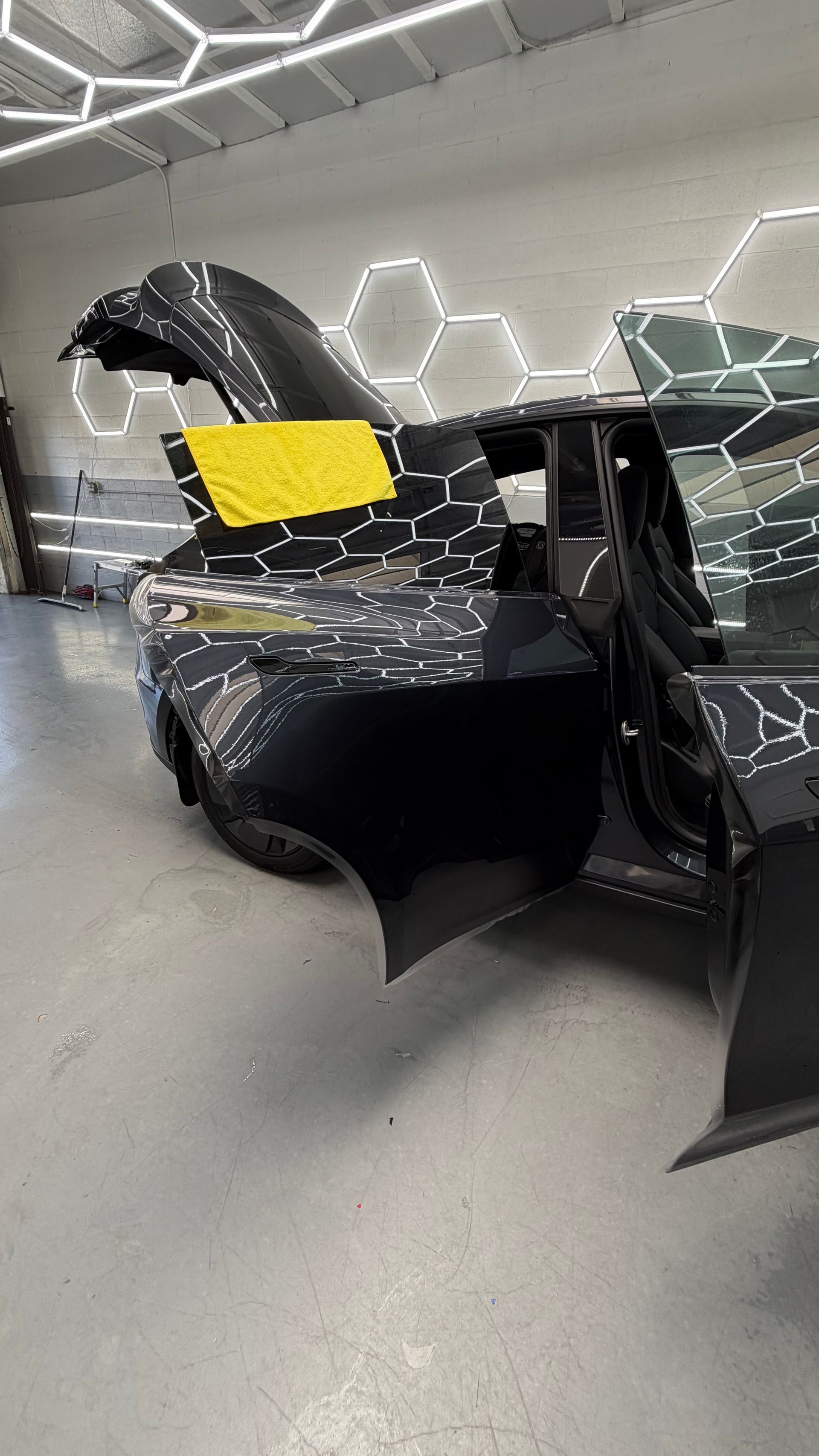 Damaged black car with broken windshield and front bumper in a garage, yellow note on windshield