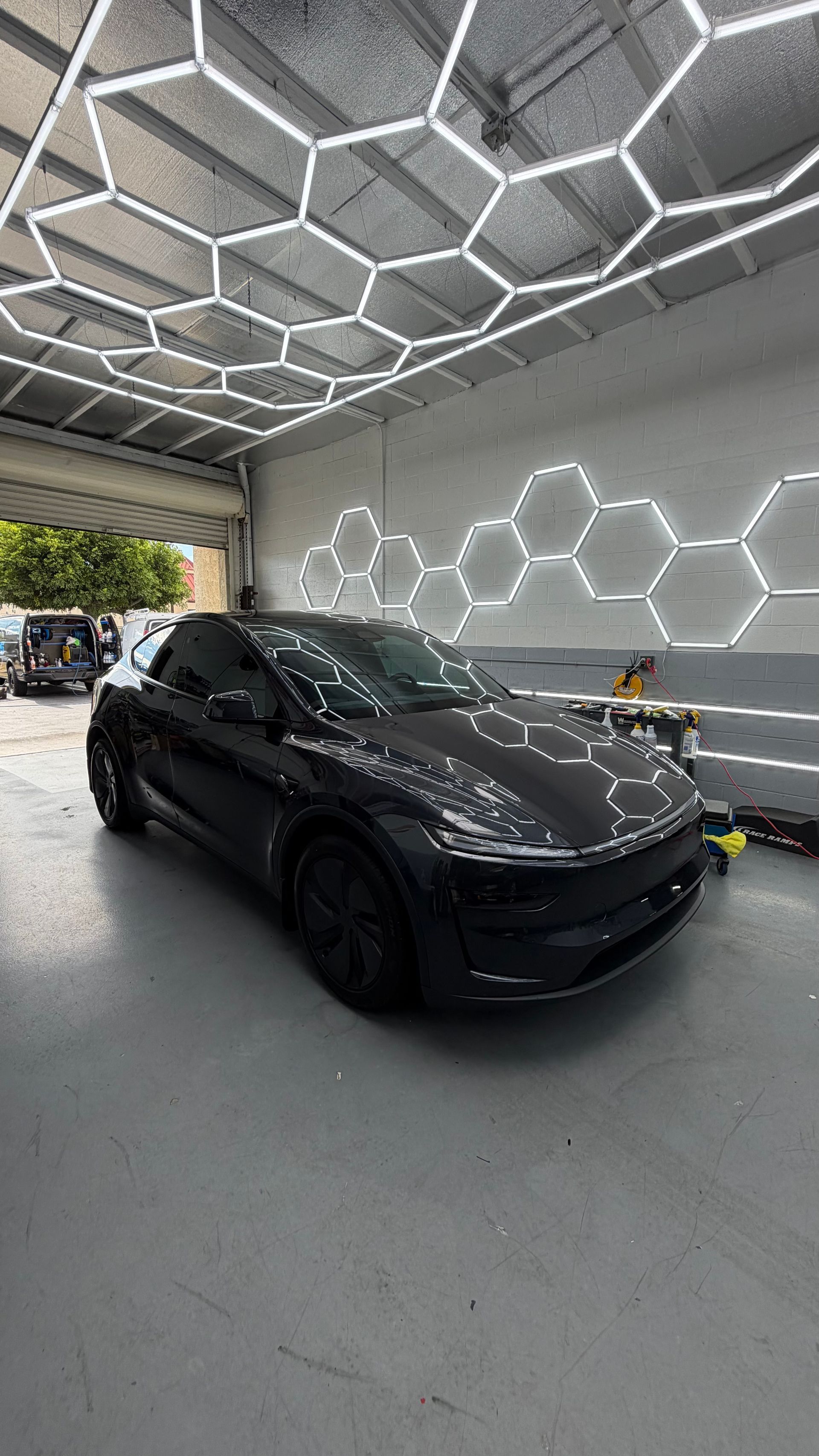 Black Tesla parked in a modern showroom with hexagonal LED ceiling lights.