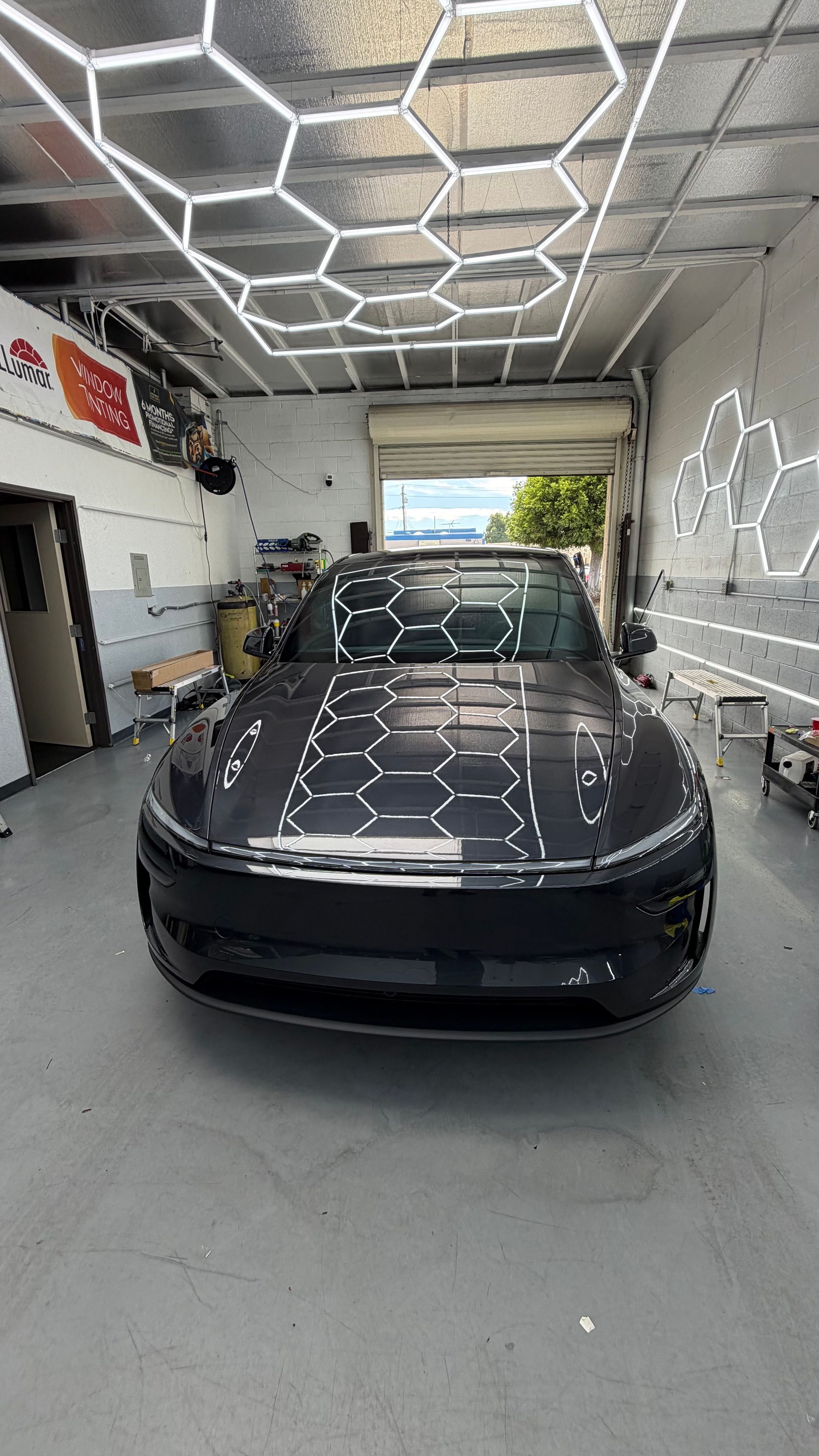 Black Tesla parked inside a garage with bright hexagonal ceiling lights