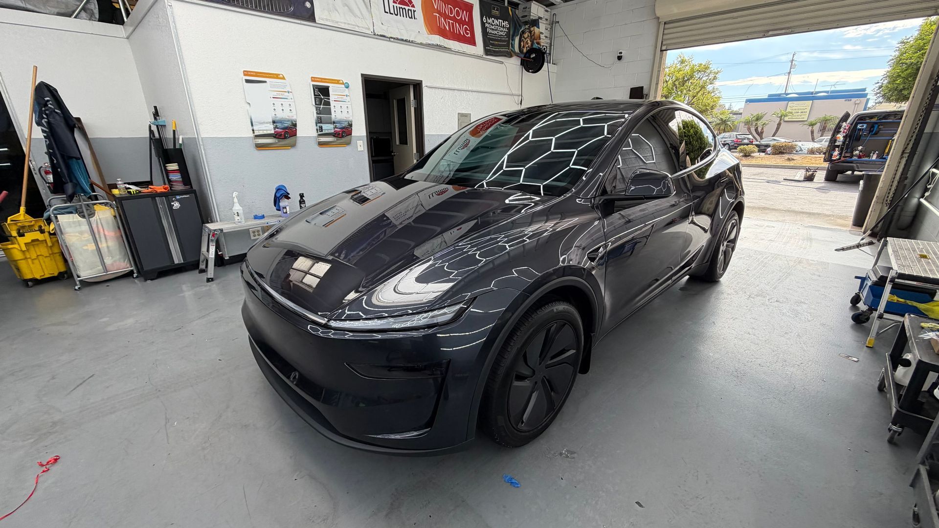 Black Tesla sedan in a garage bay with open doors and tools nearby