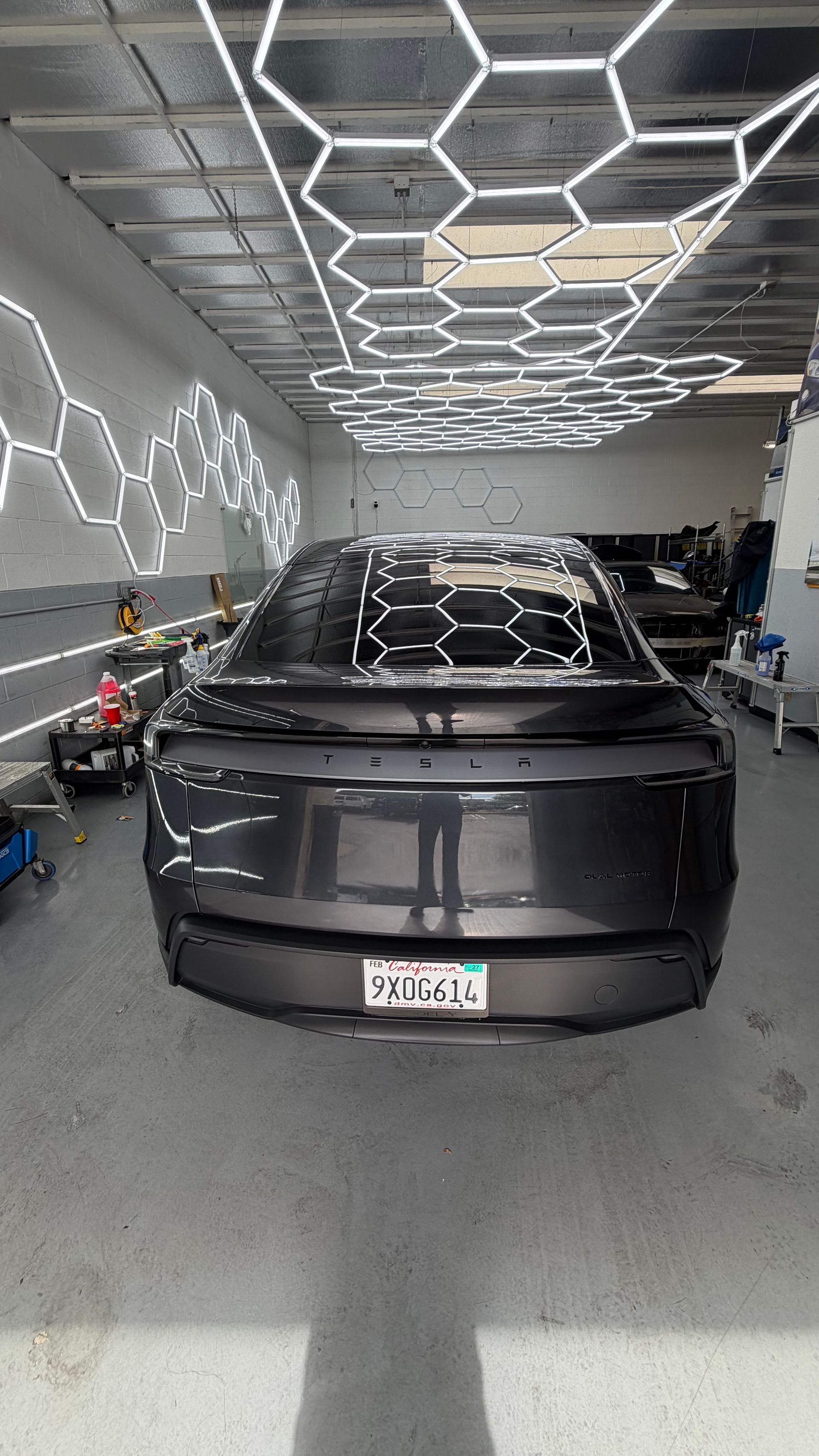 Black Tesla parked in a modern garage with geometric ceiling lights and wall lighting.