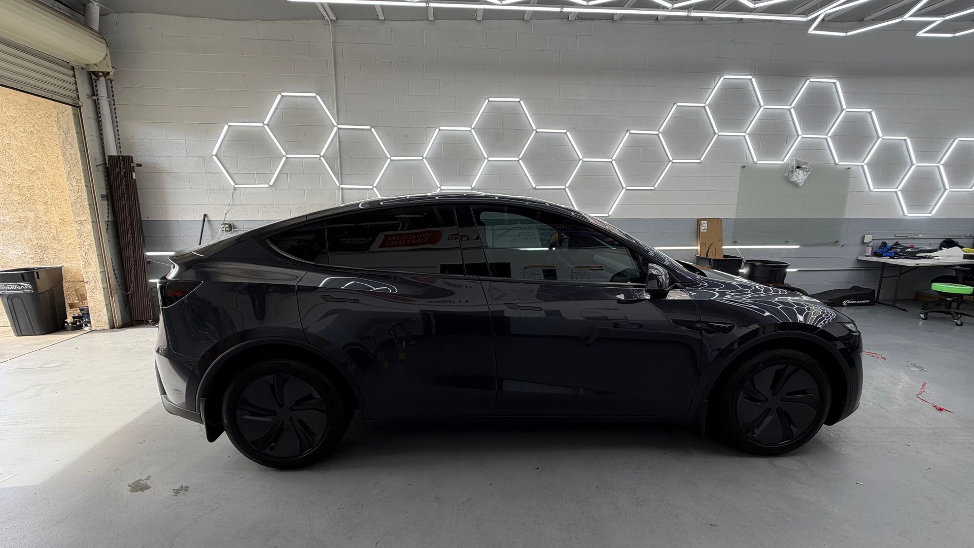 Black sedan parked indoors in a garage with hexagonal wall lights.