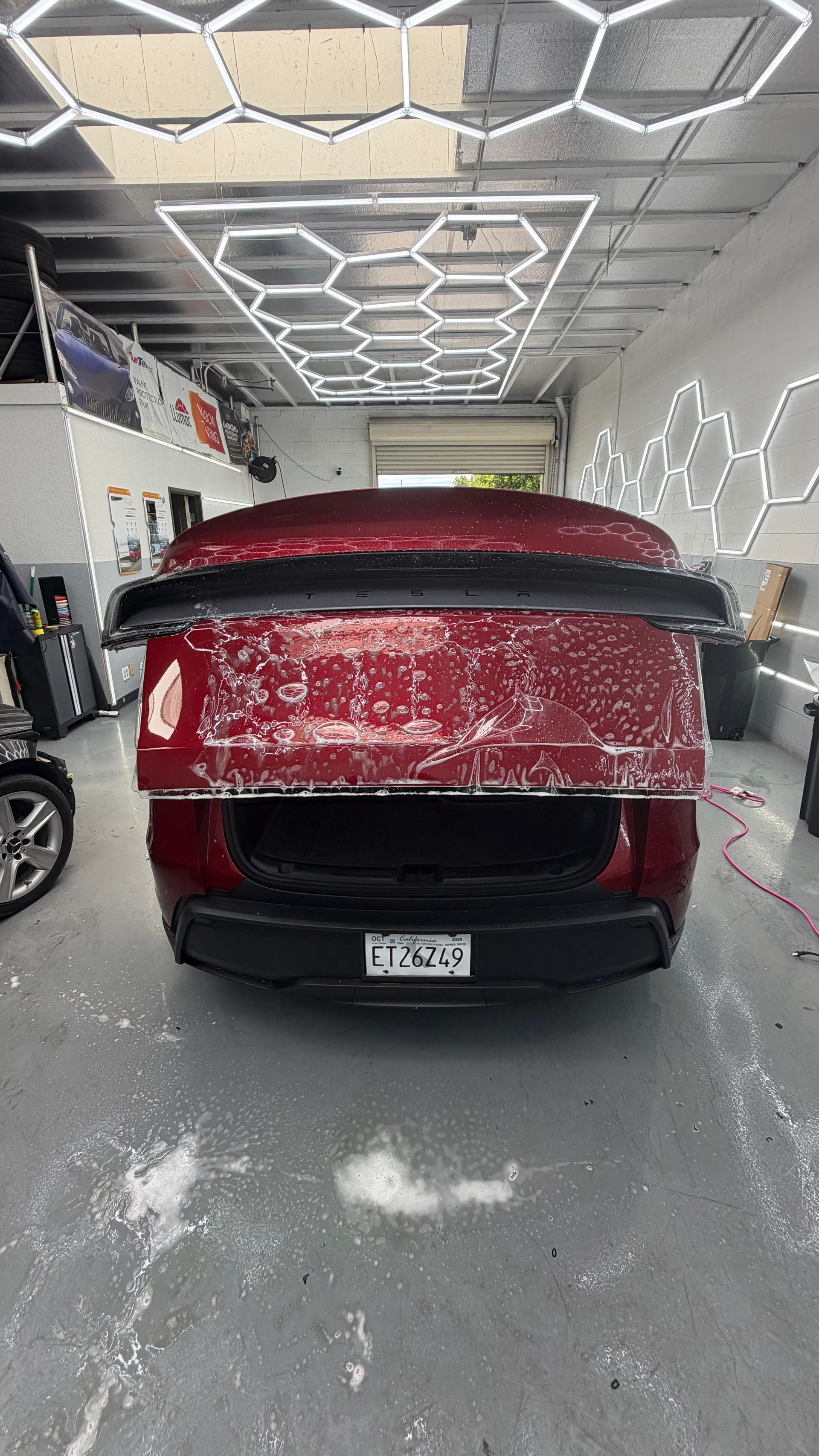 Red car in a showroom or garage, covered with a red and black protective wrap.