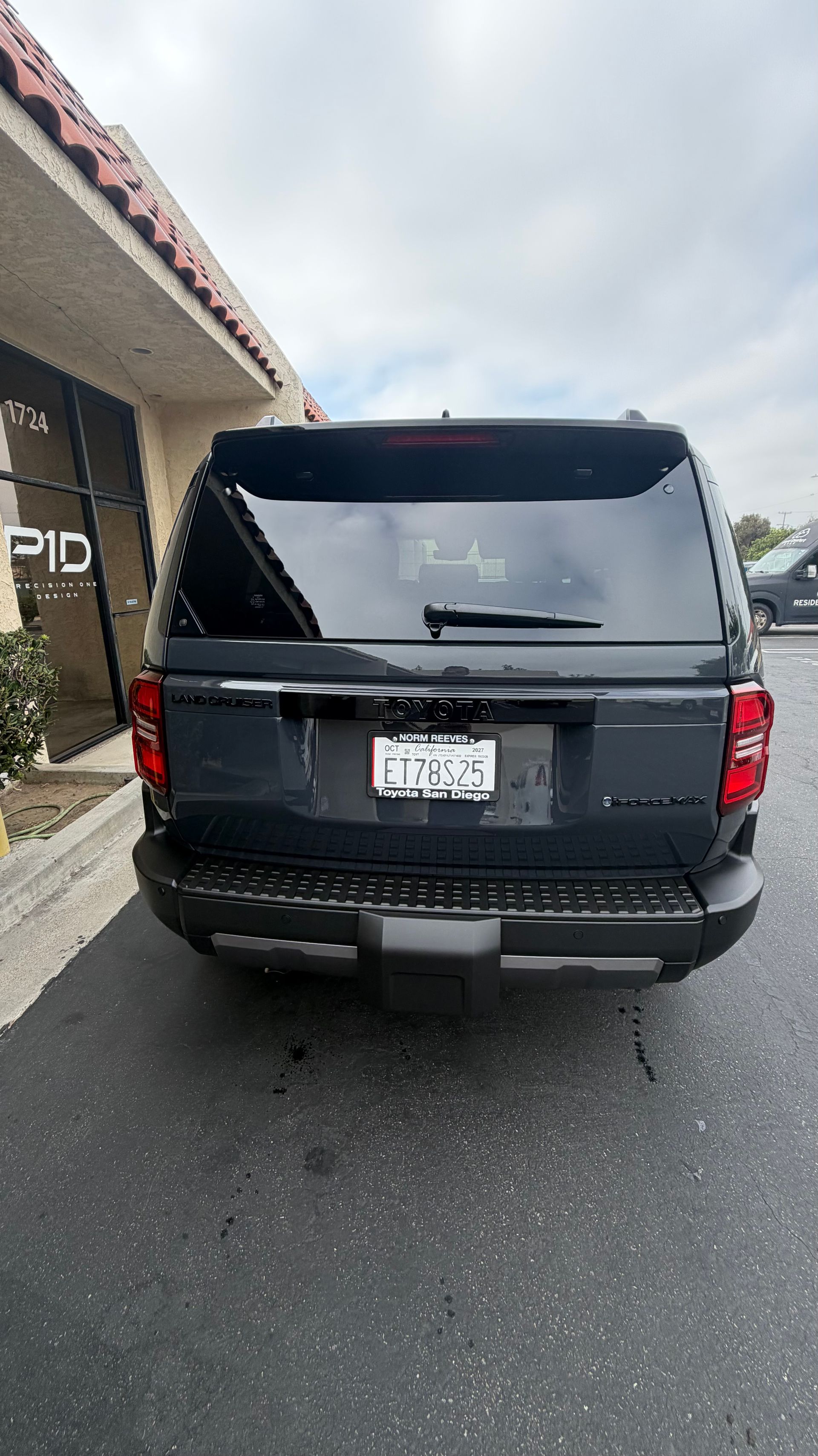 Black SUV parked in a driveway beside a building on a wet day