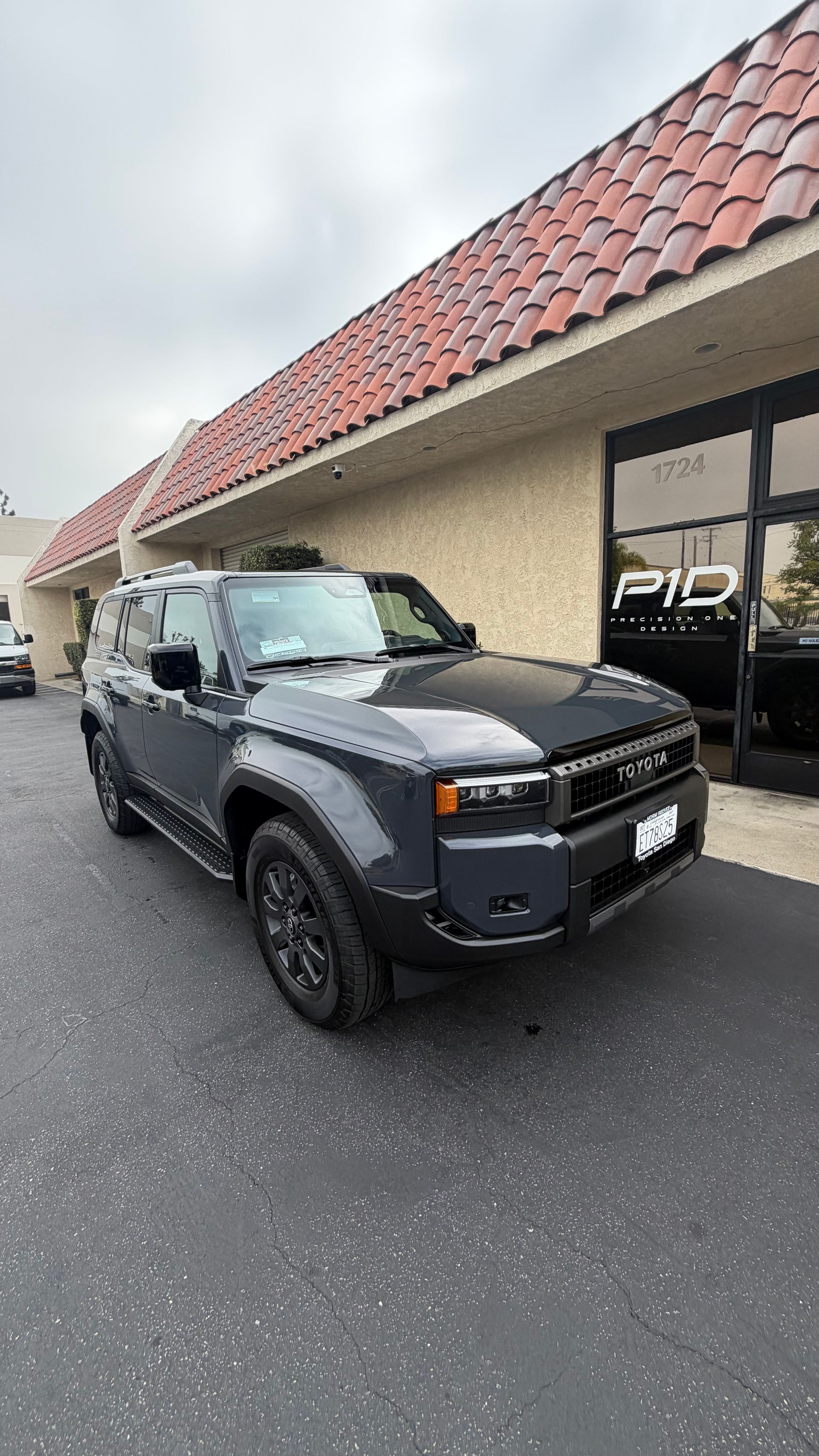 Black SUV parked outside a storefront with a red-tiled roof on a wet pavement