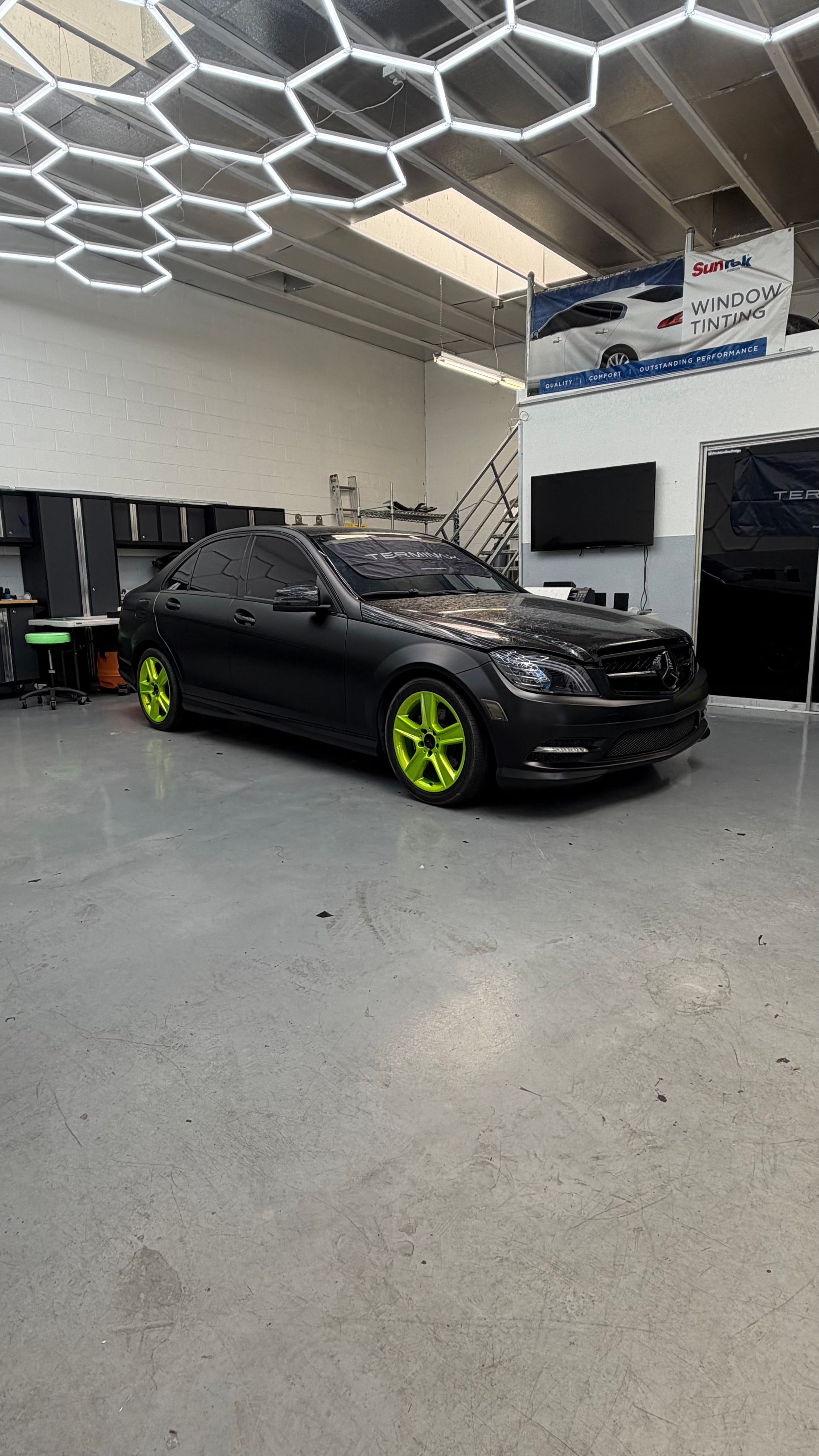 Black sports car with neon green wheels in a garage showroom under hexagonal ceiling lights
