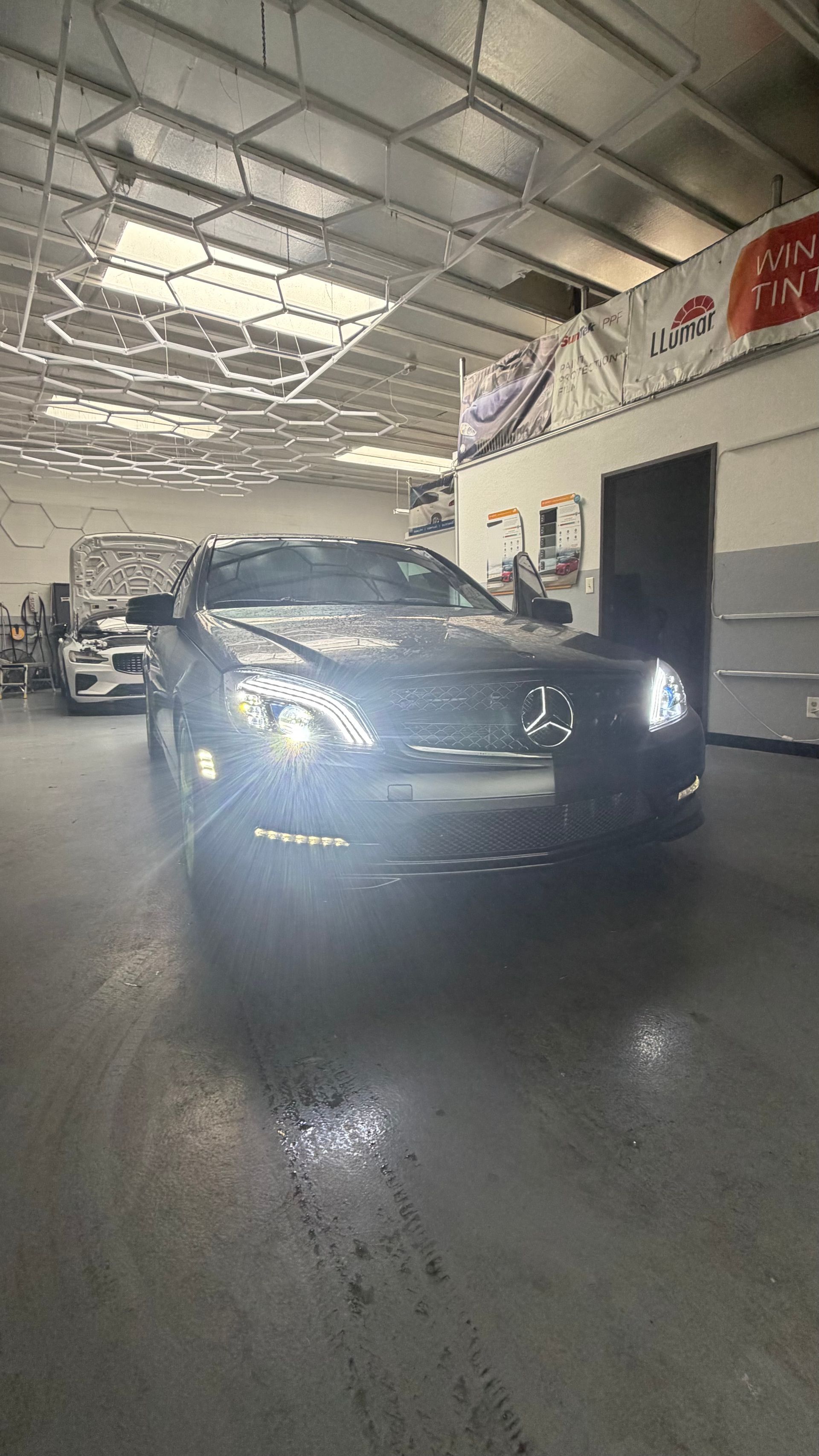 Dark blue SUV in a workshop, headlights on, with a wet floor and industrial ceiling overhead