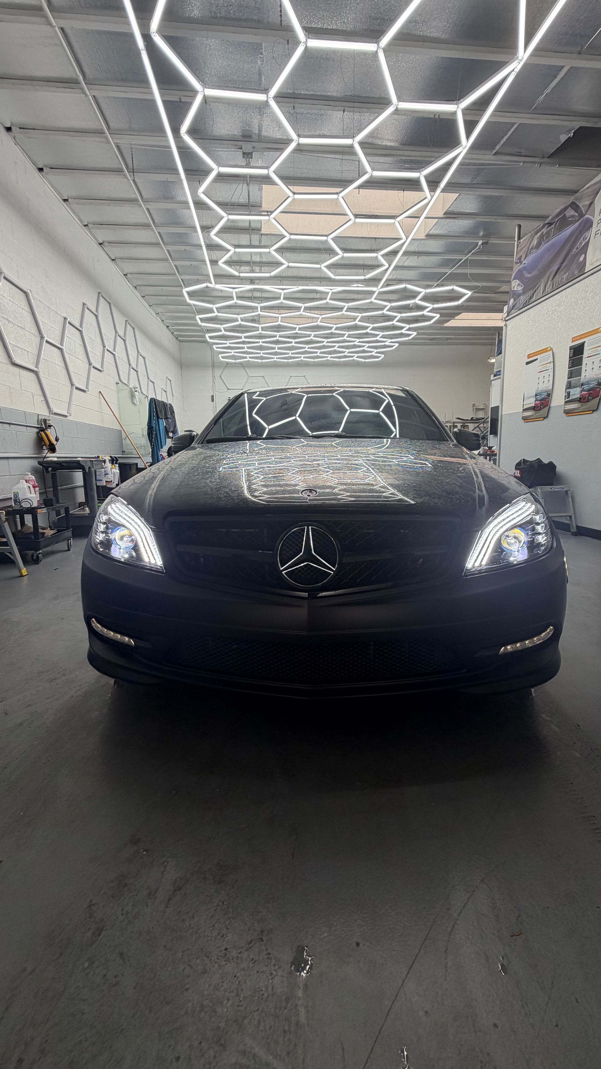 Black Mercedes-Benz sedan in a garage, viewed from the front under bright geometric ceiling lights