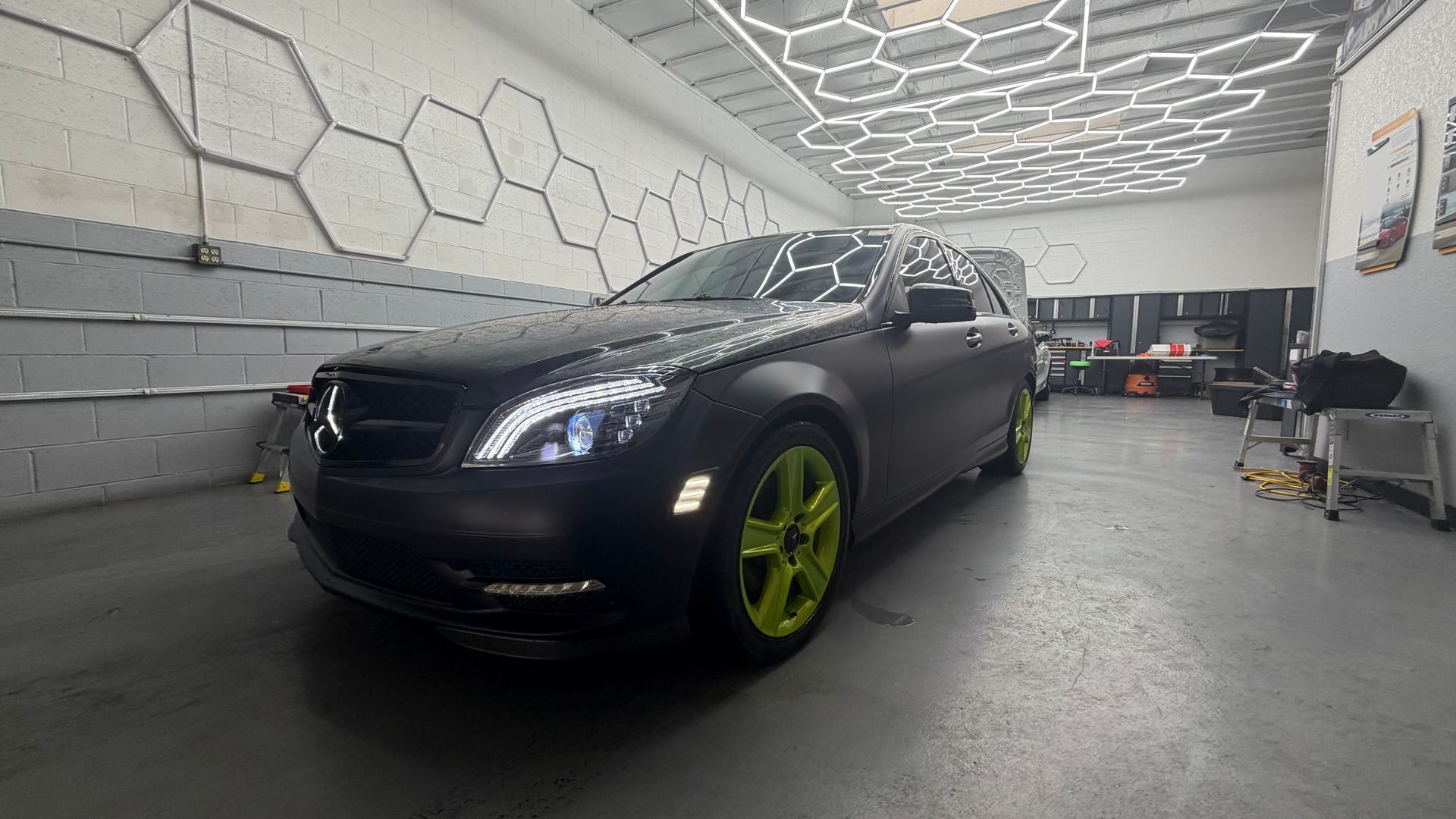 Black sedan with neon green wheels in a geometric-lit garage.