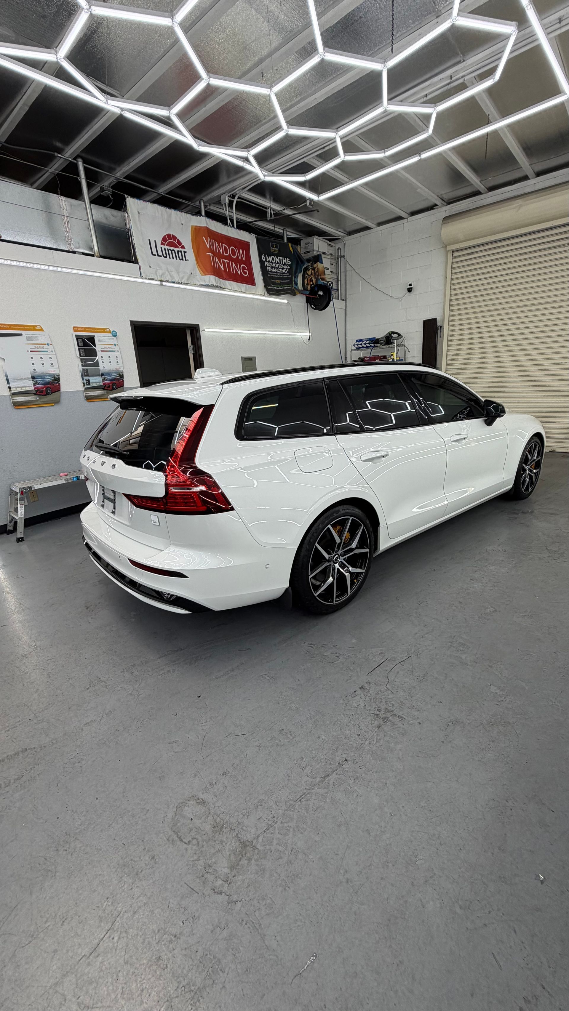 White Volvo station wagon in a clean auto shop, viewed from the rear under hexagonal ceiling lights.