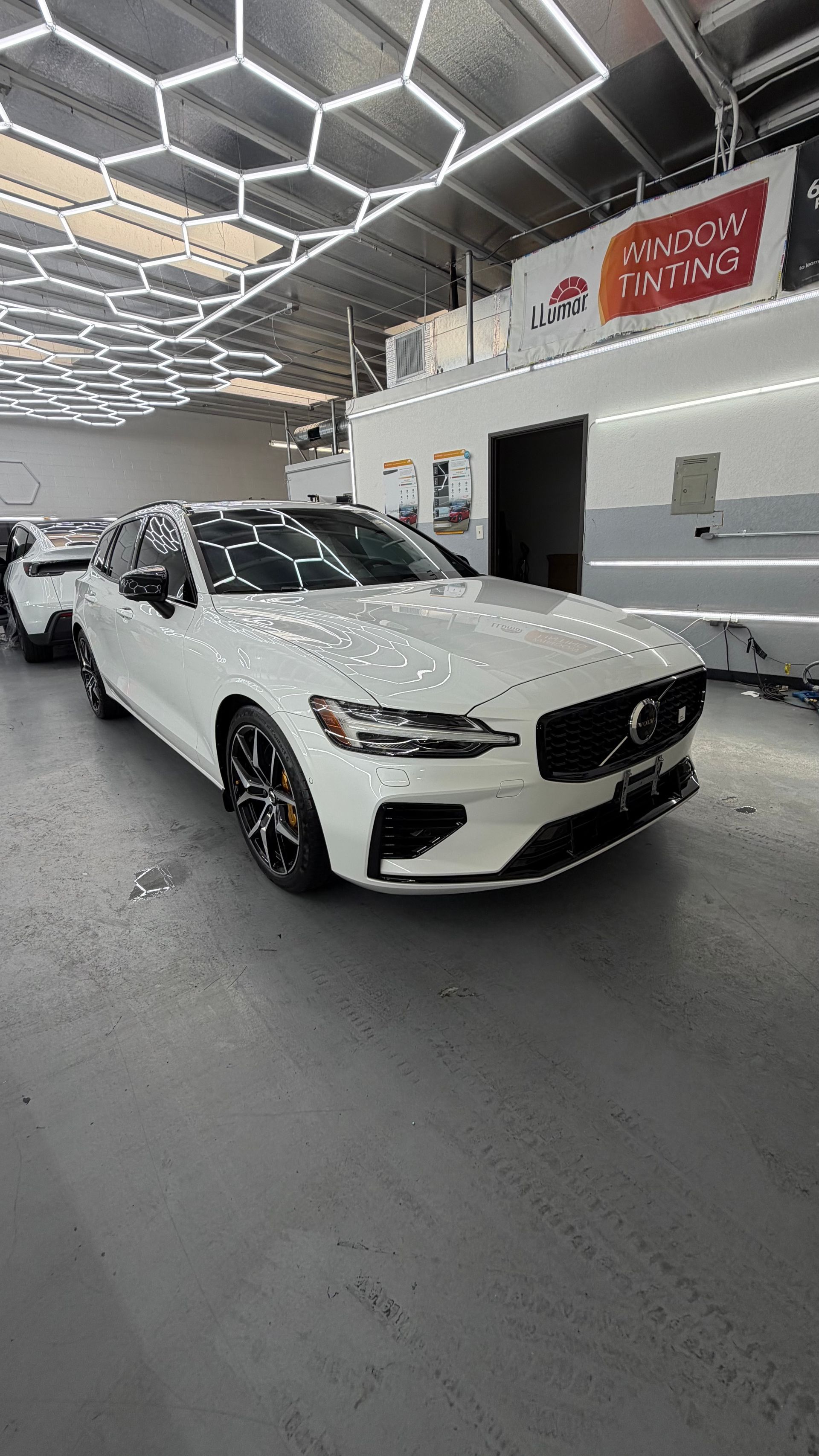 White Mercedes sedan parked indoors in a bright showroom with hexagonal ceiling lights