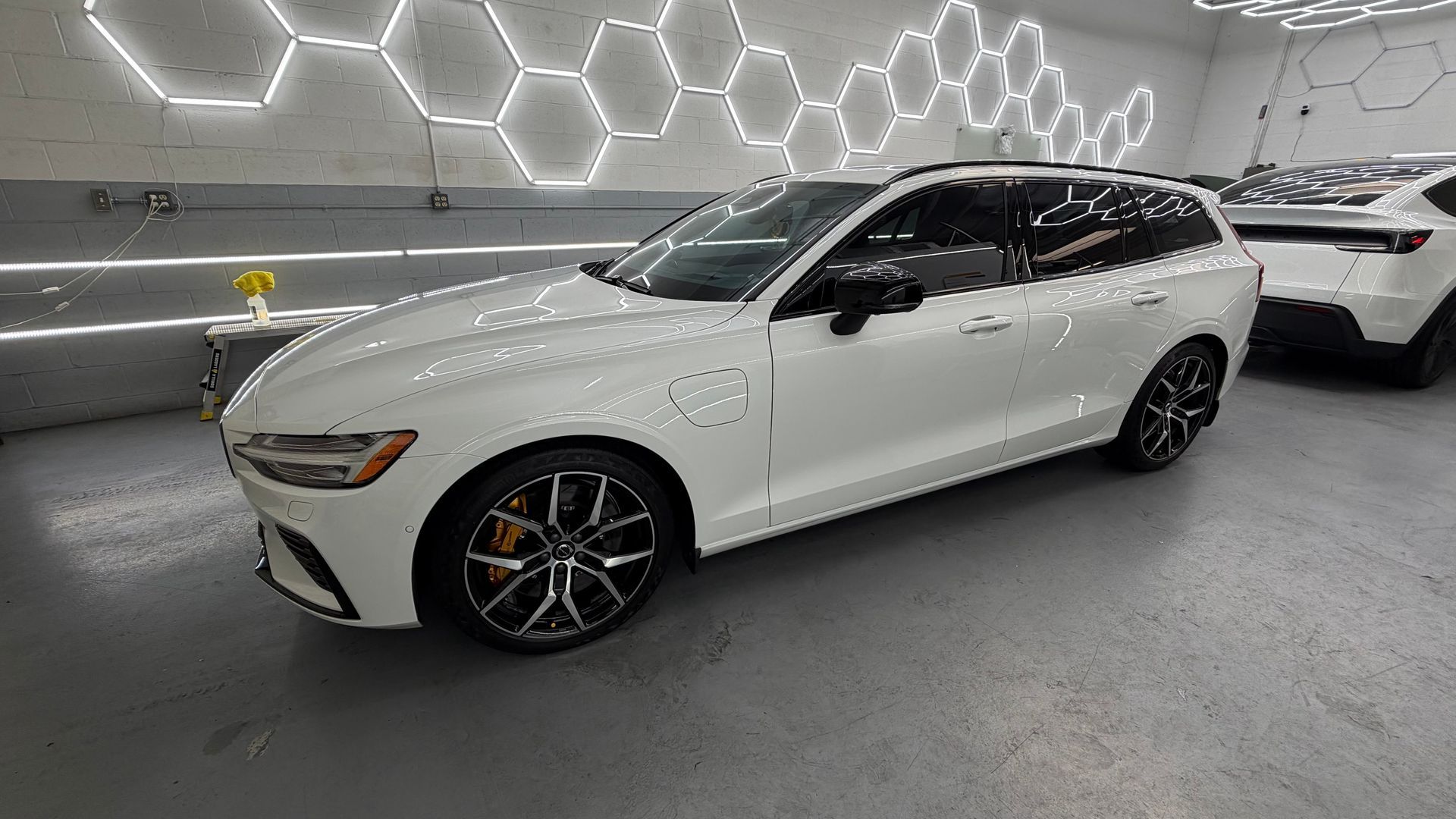 White luxury station wagon parked in a bright showroom with hexagonal ceiling lights.