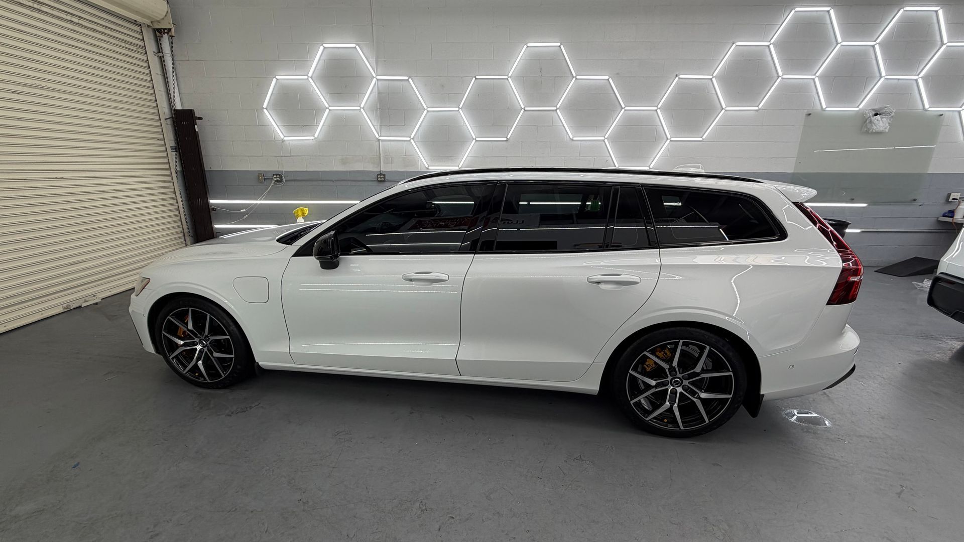 White station wagon parked indoors beside a wall with hexagonal lights and gray flooring.