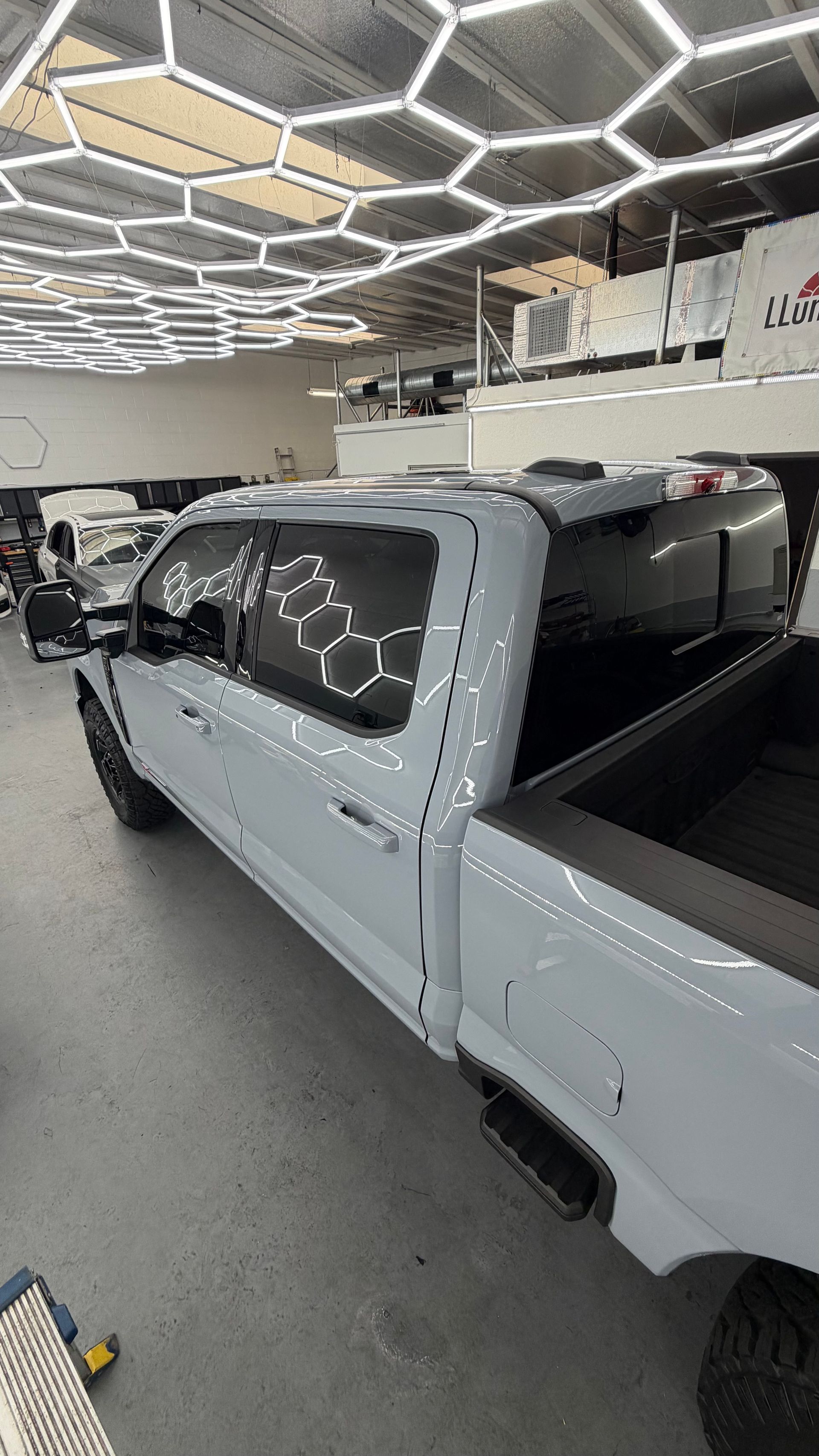 White pickup truck in a showroom with hexagonal ceiling lights reflecting on its windows.