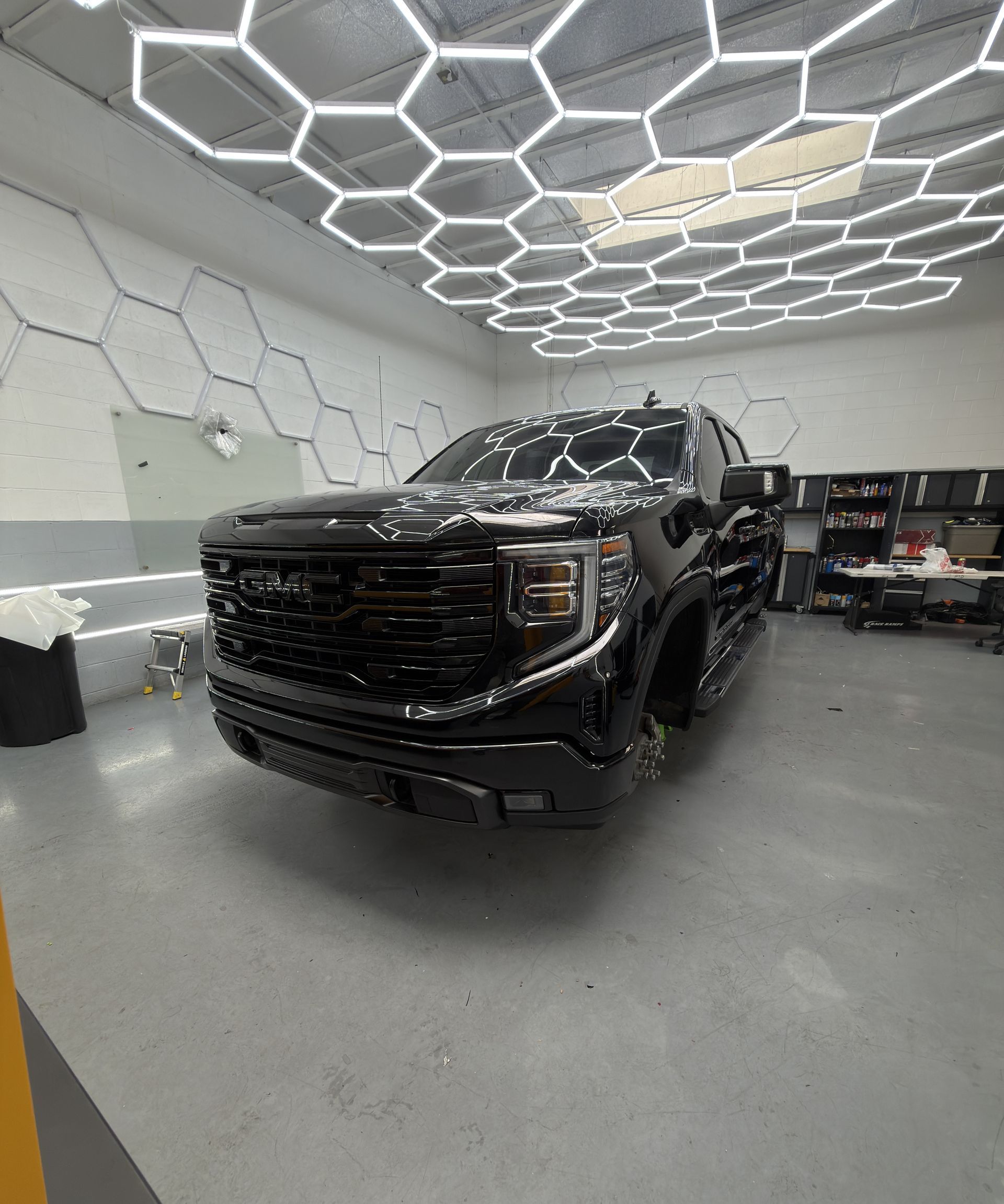Black GMC pickup truck in a modern auto shop with hexagonal ceiling lights