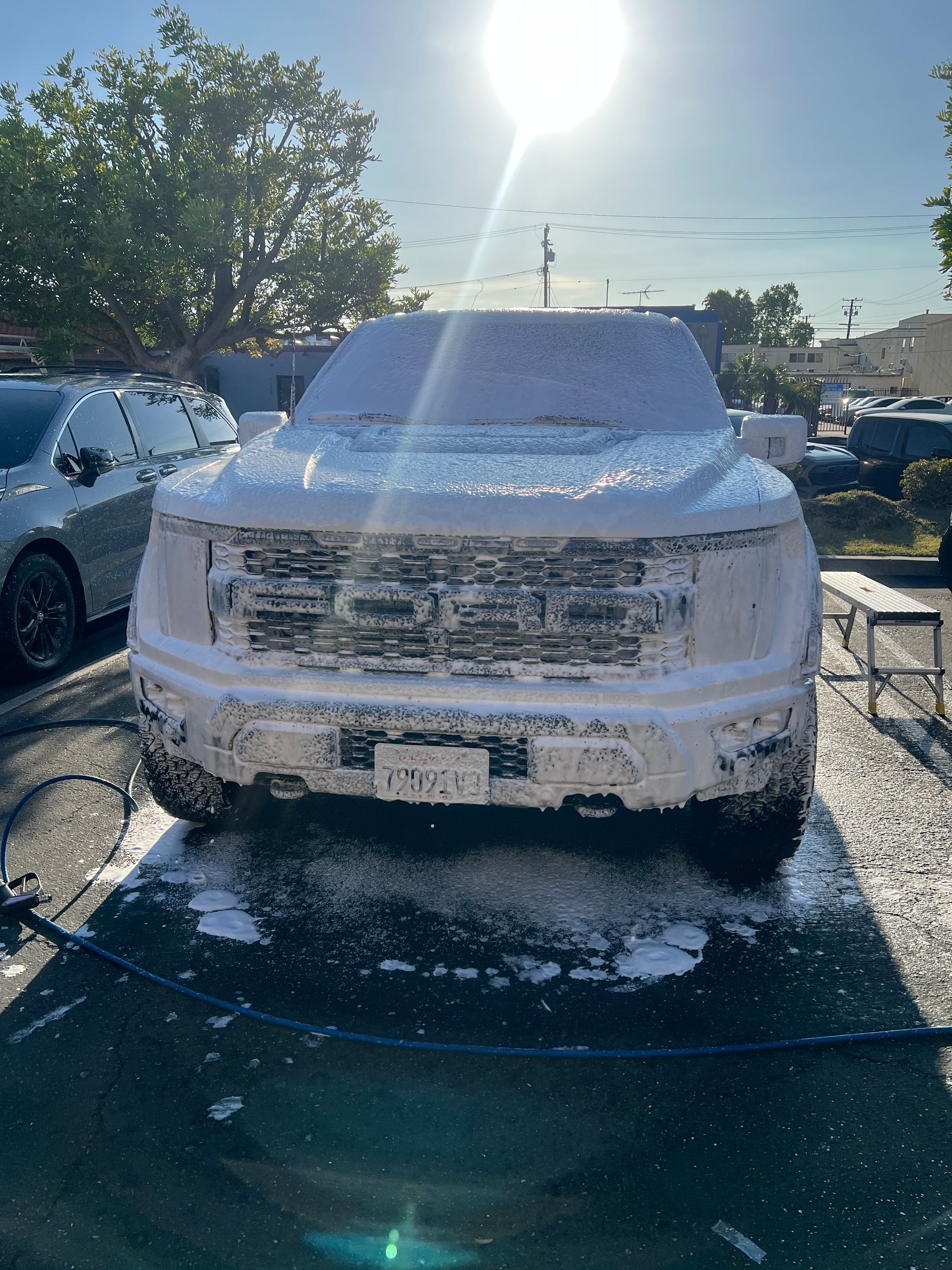 Snow-covered truck being washed outdoors in bright sunlight.