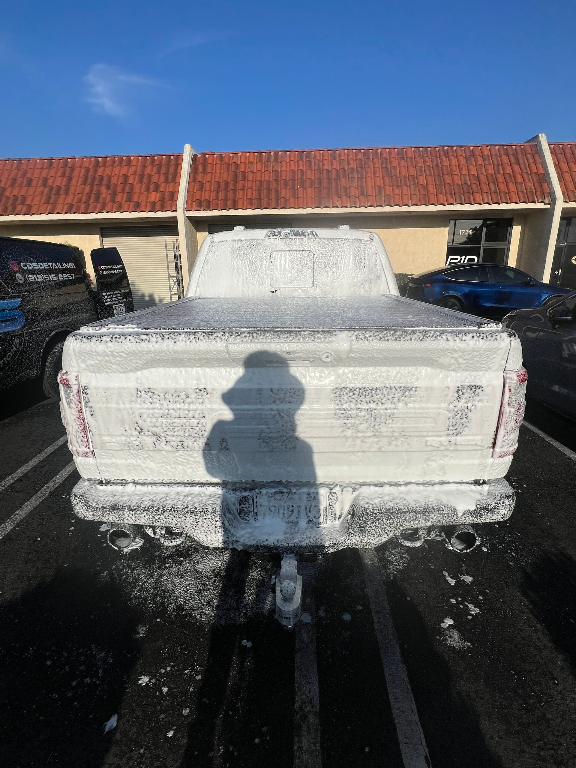 Foam-covered car in a parking lot with a person’s shadow in front of it